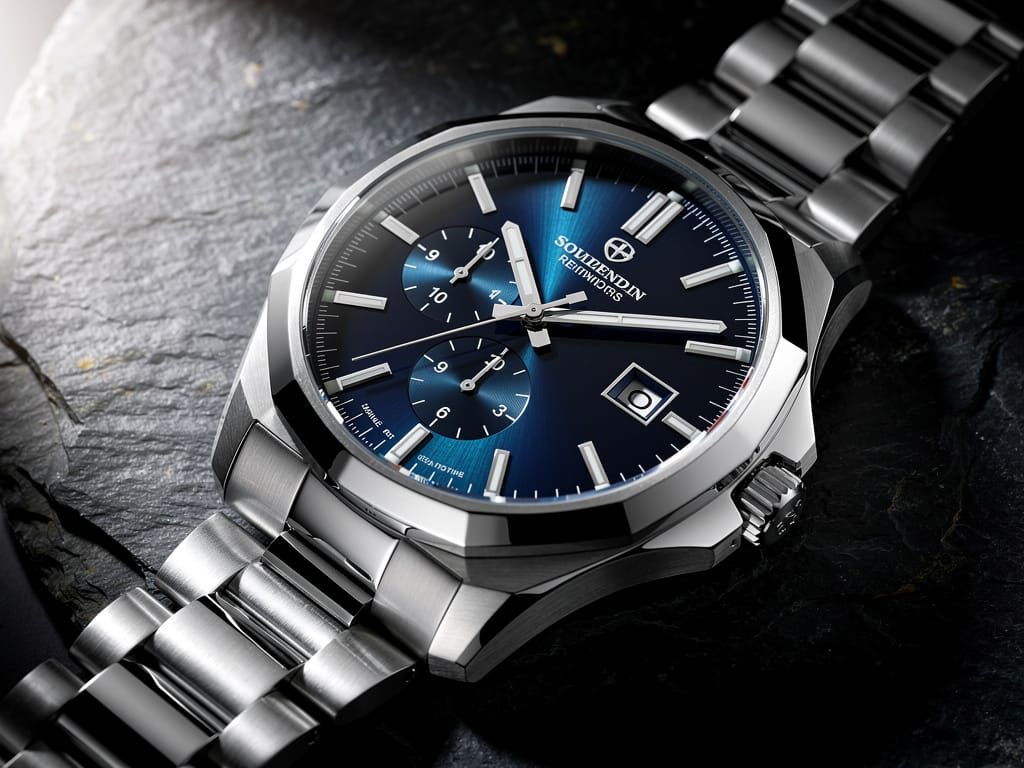 A luxury steel watch with a blue dial on a slate background