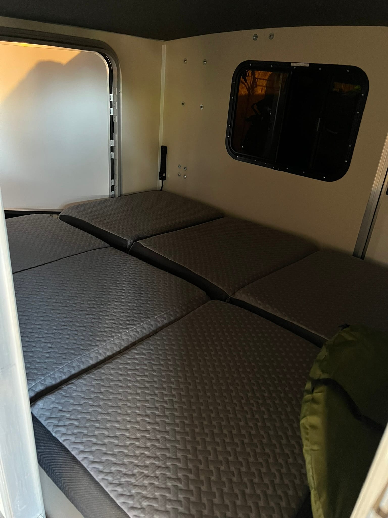 Interior of Runaway camper showing quilted gray cushions for convertible bed and small window.