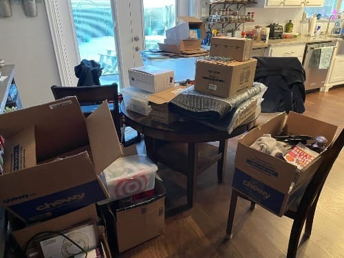 A dining area temporarily transformed by the transition process with cardboard boxes and various items spread across the table