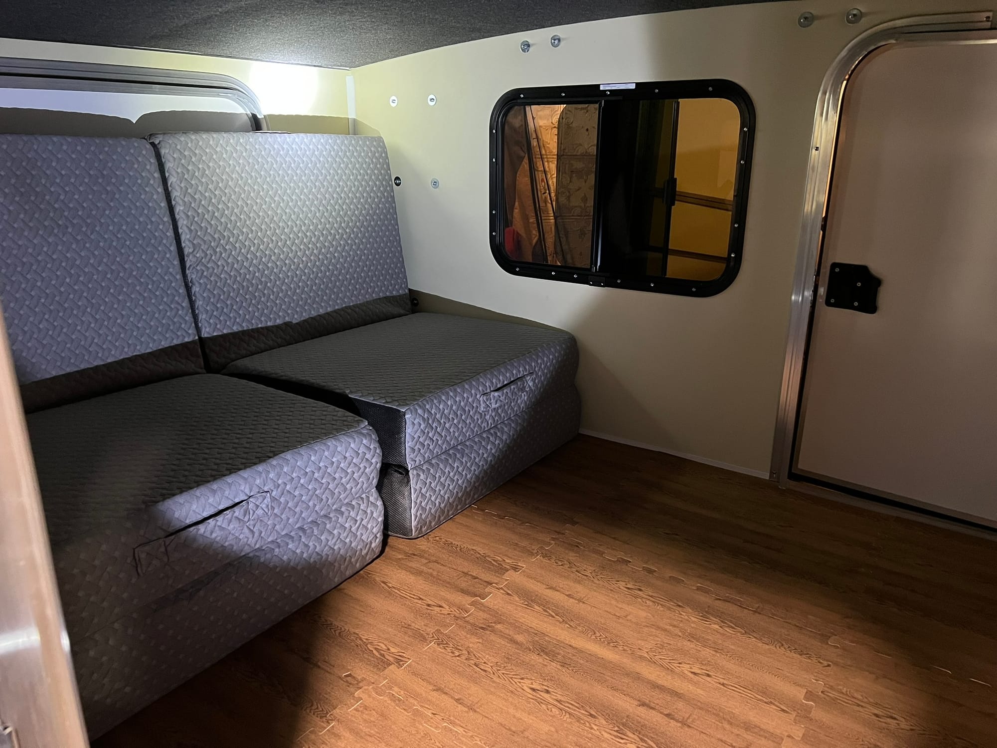 Interior of small camper showing new wood-look vinyl flooring, gray bench seating, white walls, and window, all ready for adventure.