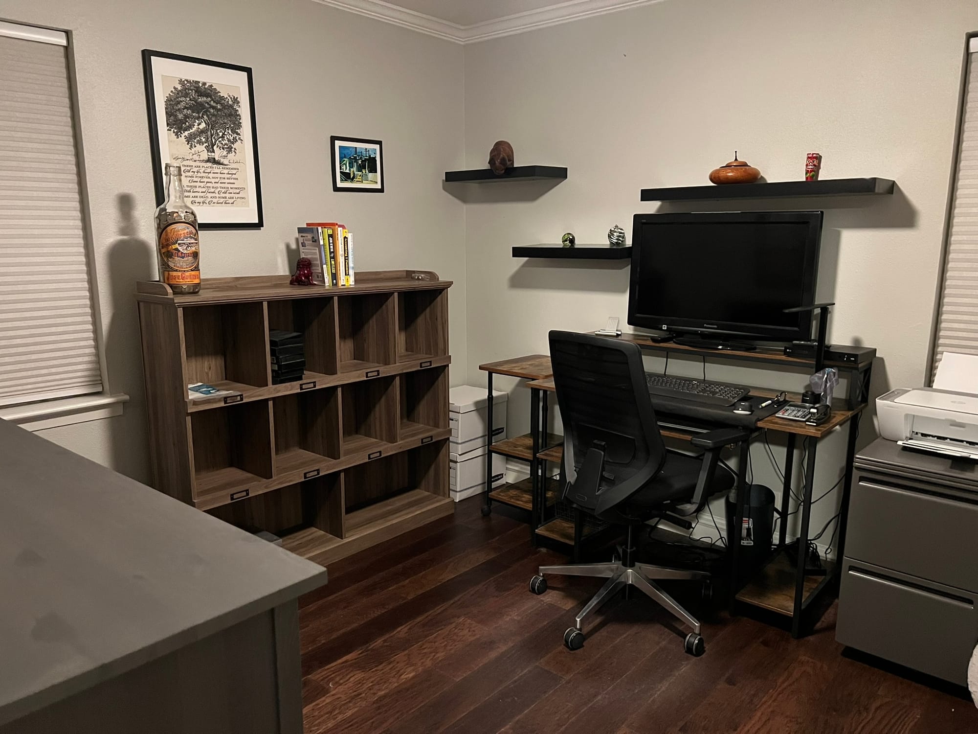 Decluttered home office with minimal personal items, nearly empty wooden cubby shelf, desk with computer monitor, and clean surfaces showing the results of the "keep only what matters" approach.