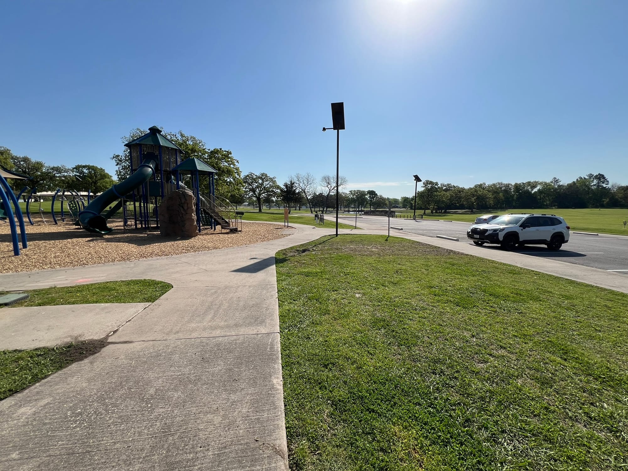A sunny day at a park with playground equipment, open green spaces, and Suby-Doo parked nearby, showing the recreational opportunities near the tiny home community.