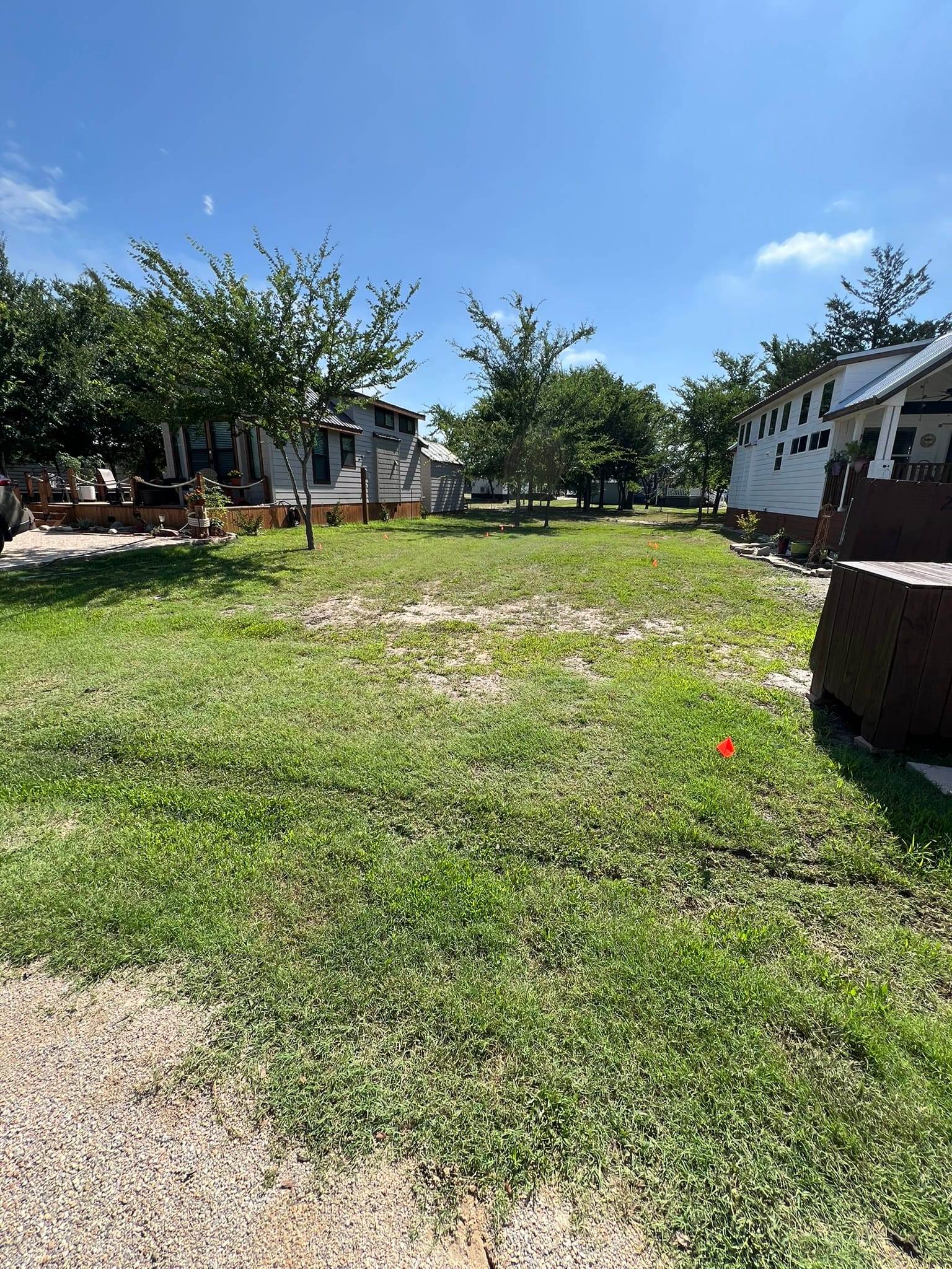 Empty lot with mature trees and scattered tiny homes visible in the background, marked for future tiny home placement.