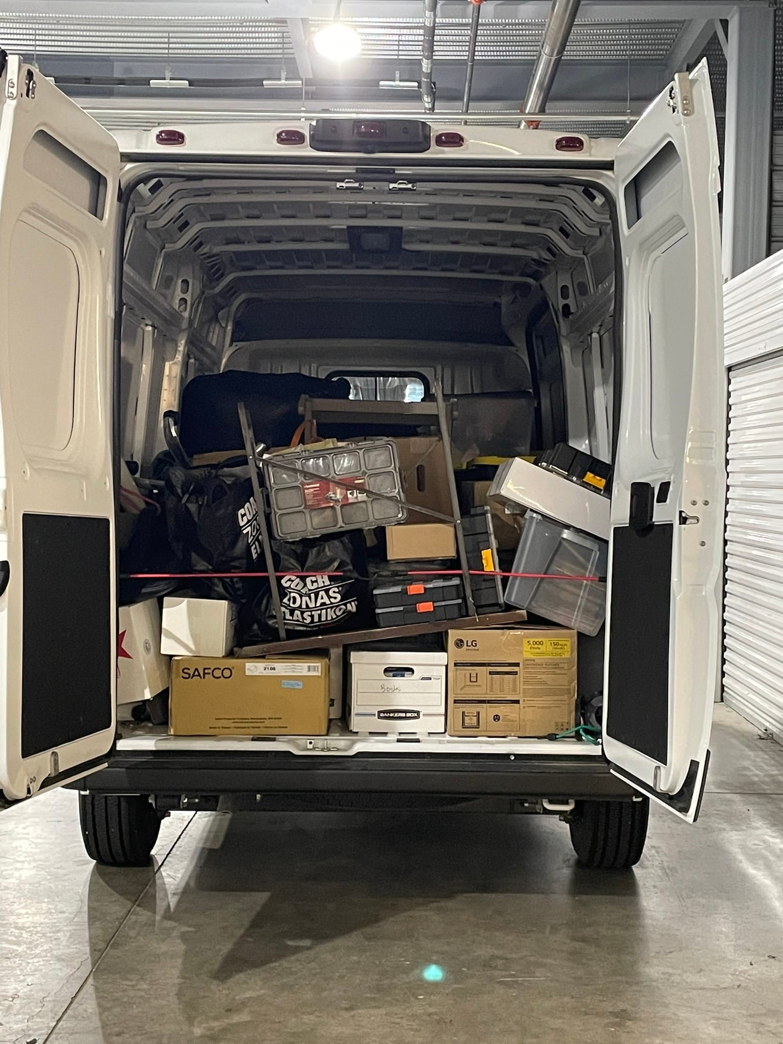 White cargo van with back doors open showing boxes and belongings loaded inside for moving to storage.