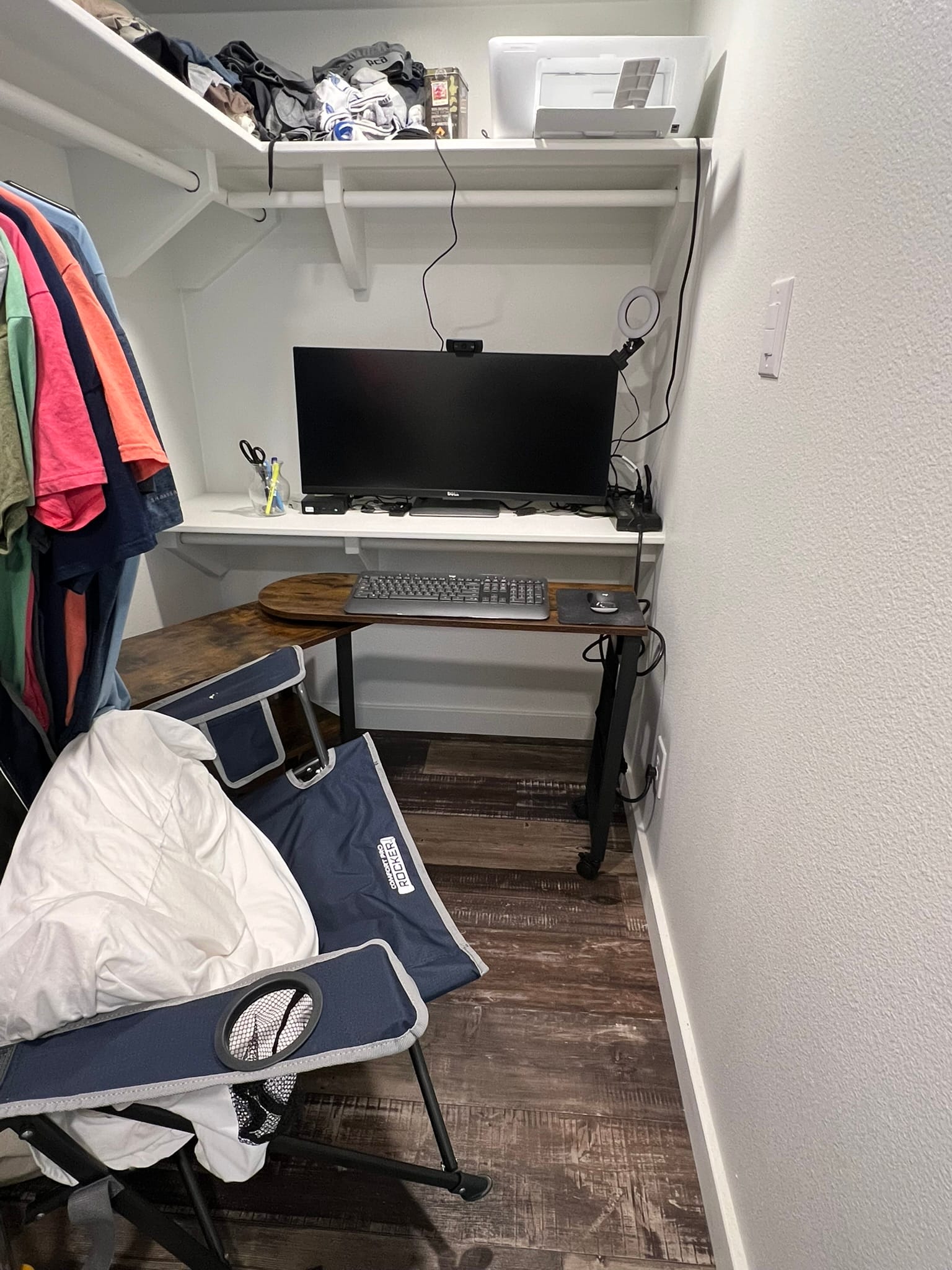 Small office setup in walk-in closet with desk, computer monitor, keyboard, and storage shelves in tiny home