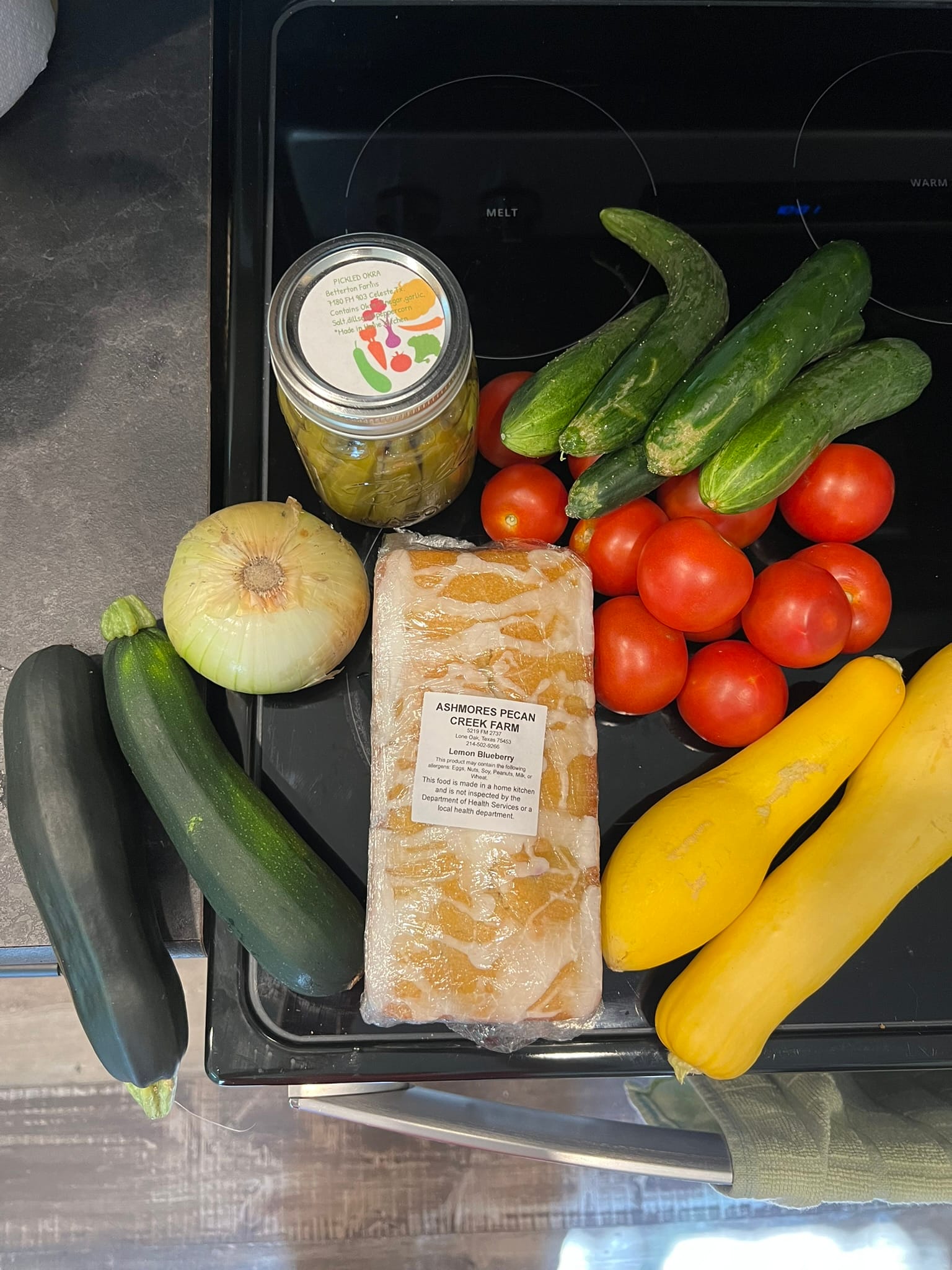 Fresh vegetables and bread from local farmer's market arranged on kitchen counter including tomatoes, cucumbers, squash, onion, and artisan bread