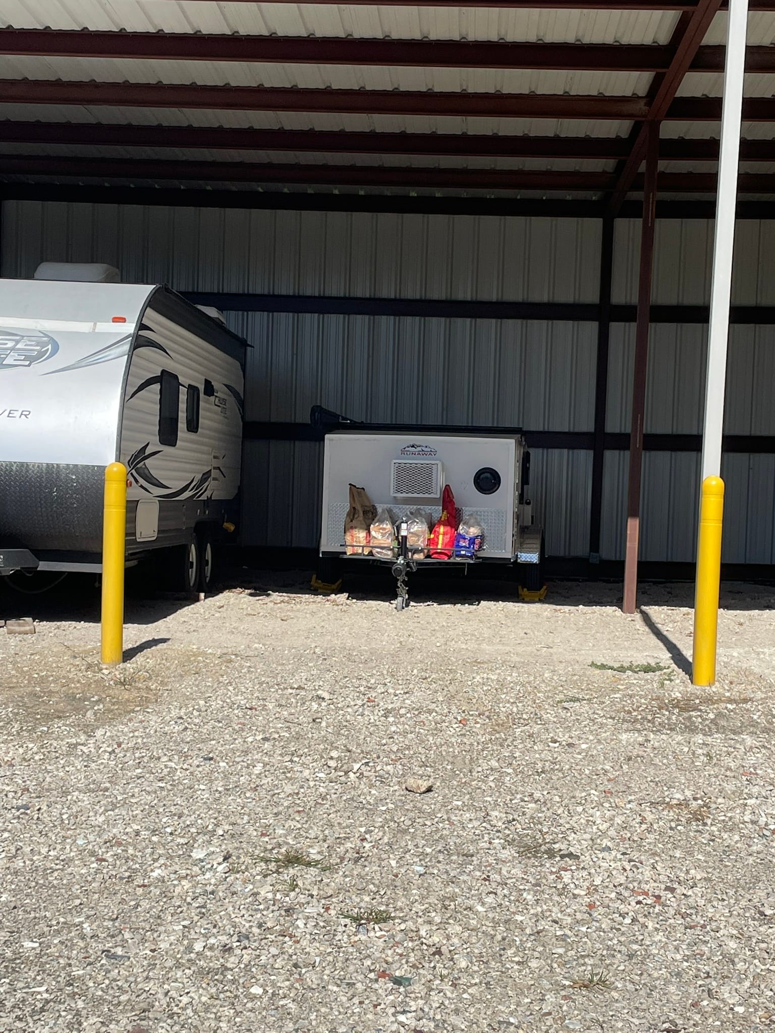 A small camper parked next to a large RV in an open storage lot, highlighting the scale difference.