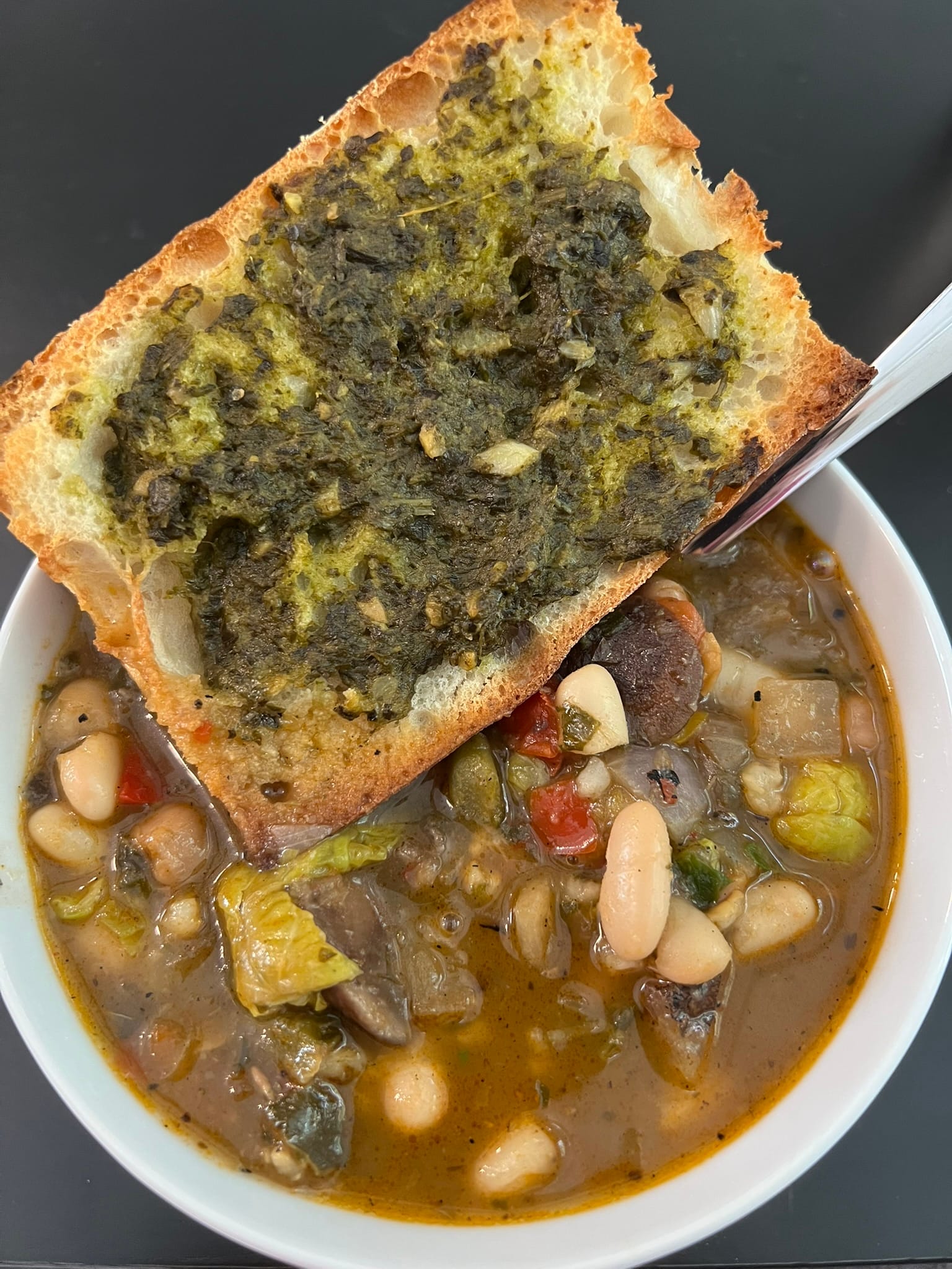 Bowl of canned vegetable soup with added cannellini beans and diced tomatoes, served with toasted bread and pesto spread