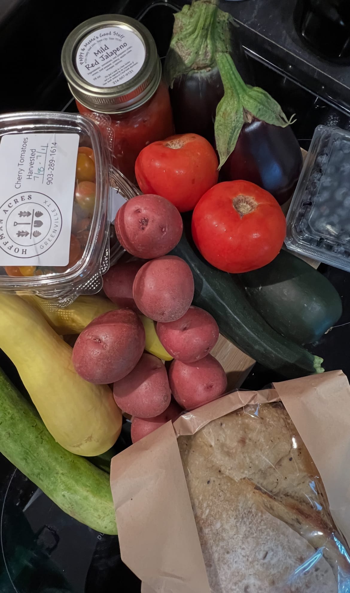 Portrait image of fresh produce from a North Texas farmers market: tomatoes, cucumbers, blueberries, and artisan sourdough bread