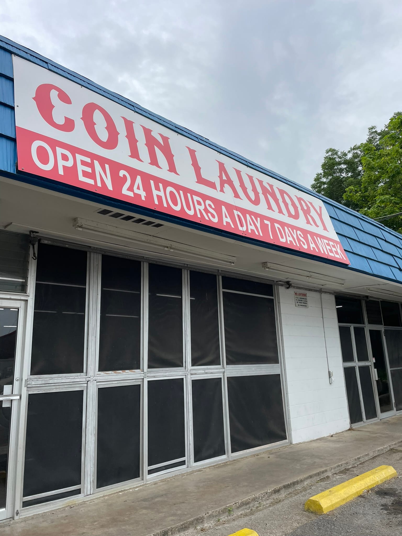 A photo of the exterior of a coin-operated laundromat with a sign that says, "COIN LAUNDRY OPEN 24 HOURS A DAY 7 DAYS A WEEK."
