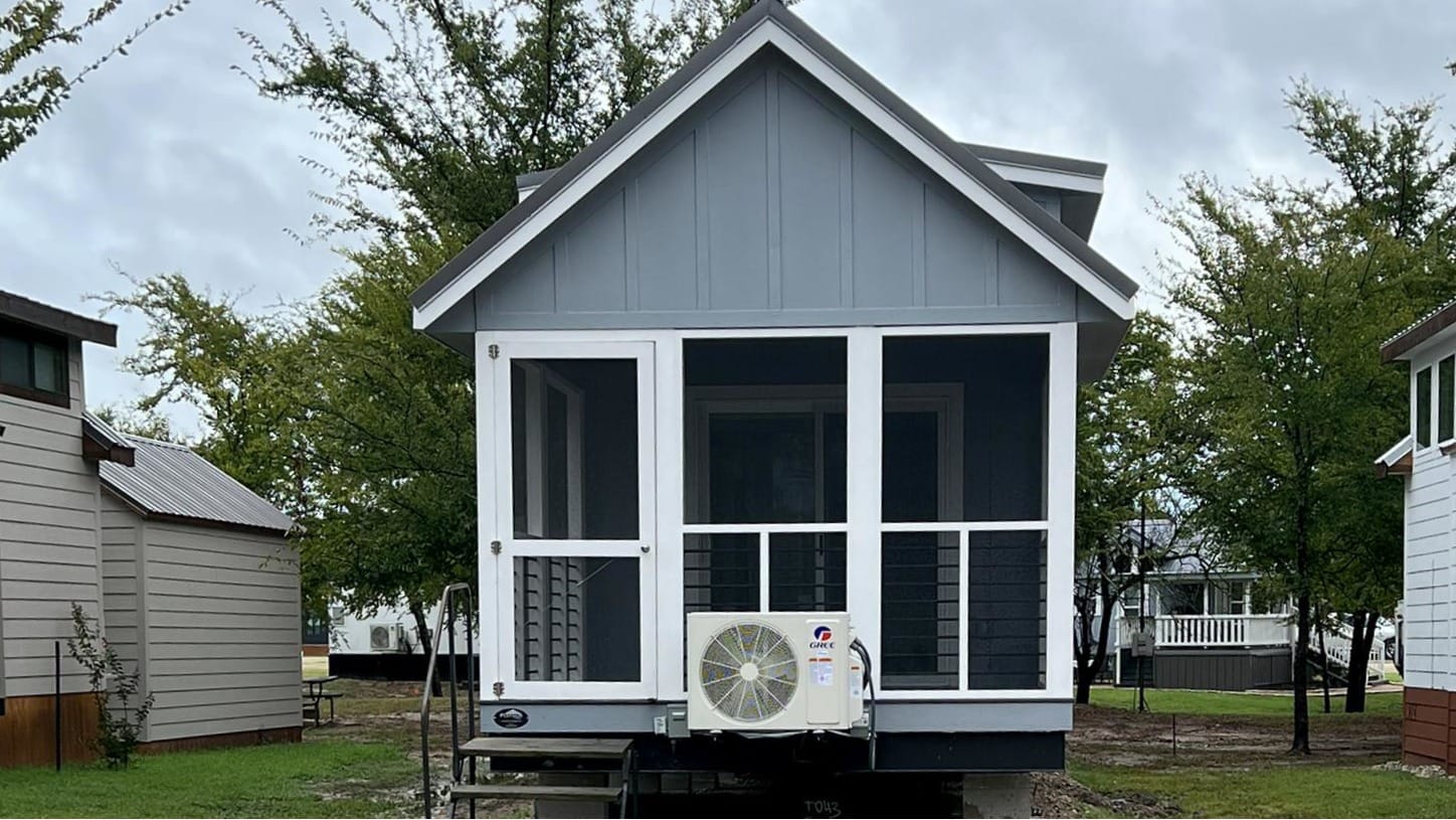 Gray tiny house with screened porches now properly positioned on gravel pad between neighboring homes