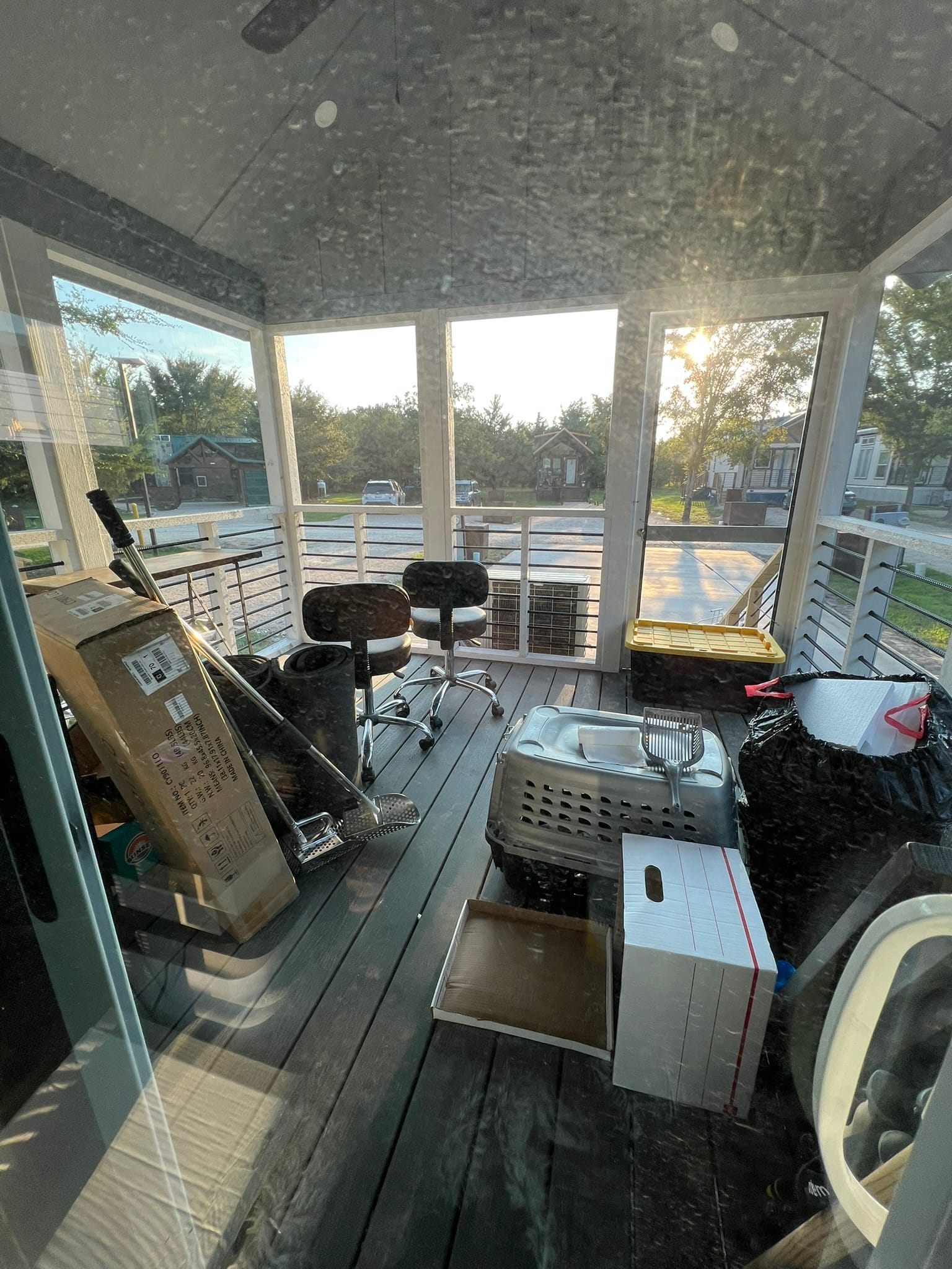 Screened porch filled with moving boxes, office chairs, and various items during tiny house moving process