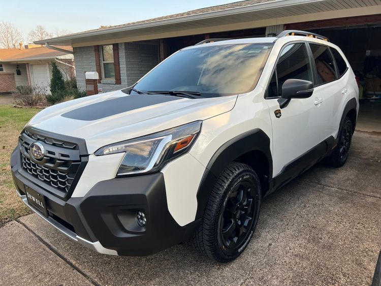 2024 Subaru Forester Wilderness in pearl white with black trim and wheels, parked in driveway showing adventure-ready styling