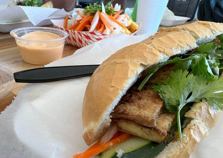 Vietnamese banh mi sandwich with tofu and fresh vegetables on crusty bread, served with pickled vegetables and sauce at a local restaurant.