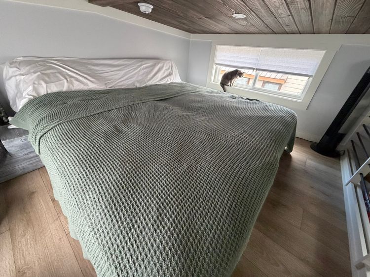 Completed king-size bed in tiny house loft with green blanket, showing successful bedroom setup with adequate headroom clearance