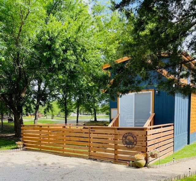 Blue tiny house with wooden deck surrounded by trees in a peaceful community