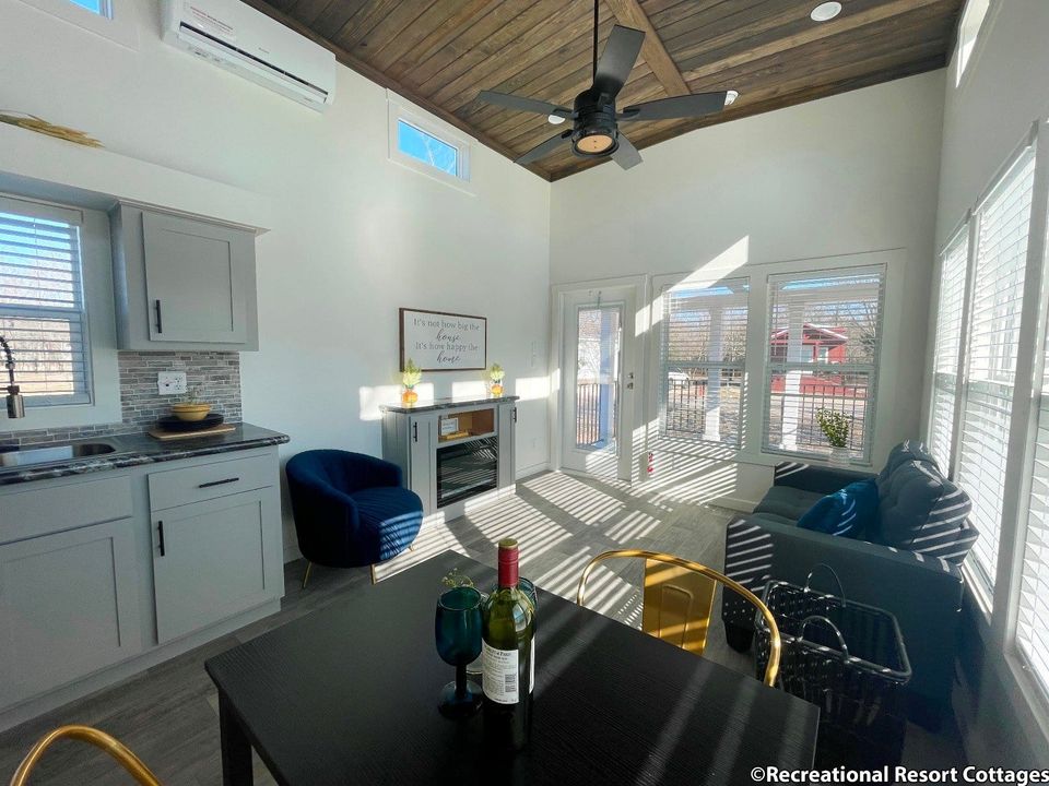 Interior view of a tiny home with white cabinets, wooden ceiling, open concept living area with kitchen, dining space and living room with doors to porch.