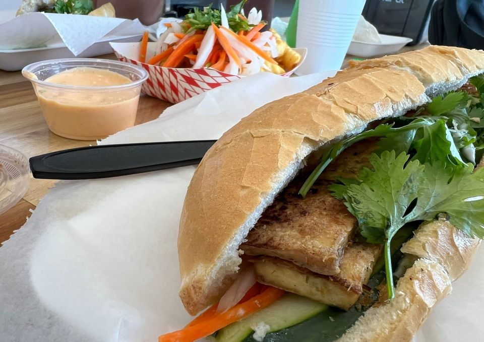 Vietnamese banh mi sandwich with tofu and fresh vegetables on crusty bread, served with pickled vegetables and sauce at a local restaurant.
