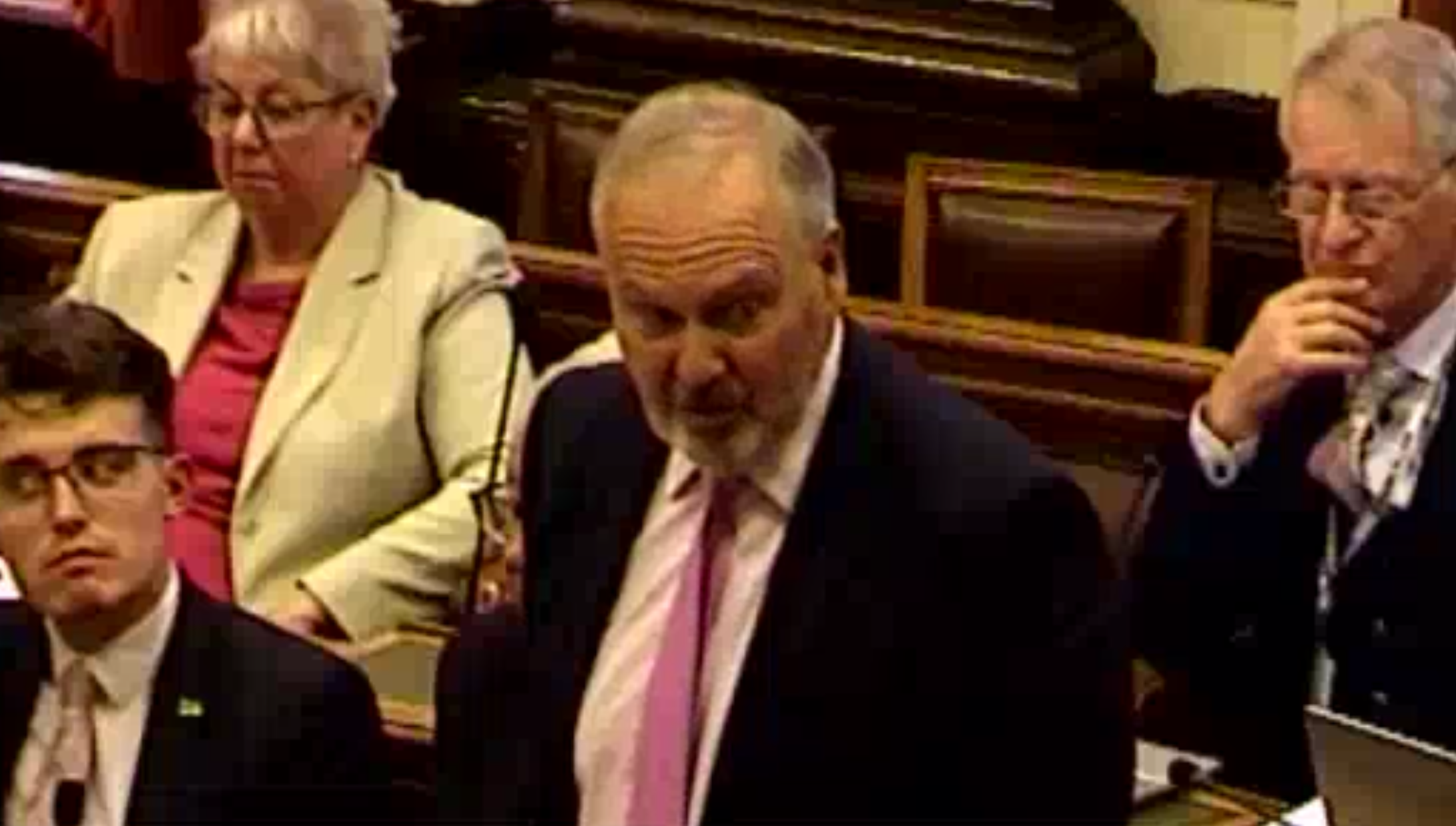 Screenshot from Wirral Council video of Cllr Moutney speaking at the meeting. He is stood up in the chamber and behind him are four conservative councillors.
