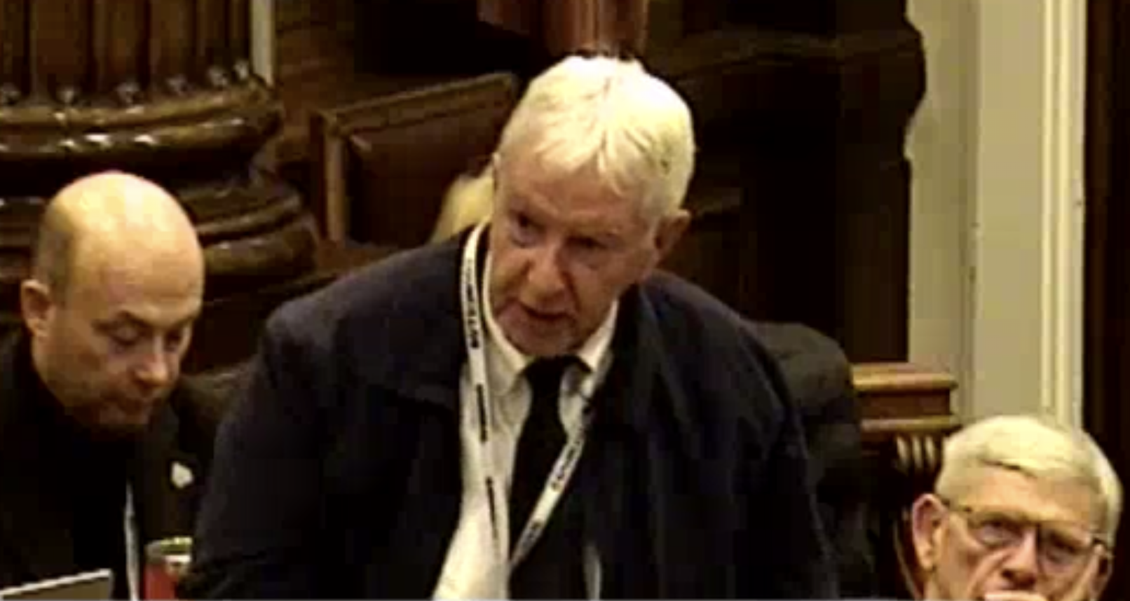 Screenshot Image from Wirral council video of Cllr Murphy speaking at the meeting. He is standing, behind him, seated are two Labour councillors