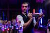 Male Bartender Shaking Cocktail Mixer With Rolled Up Sleeves Unaware Of How Much Power He Has
