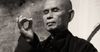 Portrait of Thich Nhat Hanh holding a mudra, a hand gesture with the third finger bent and held by the thumb.