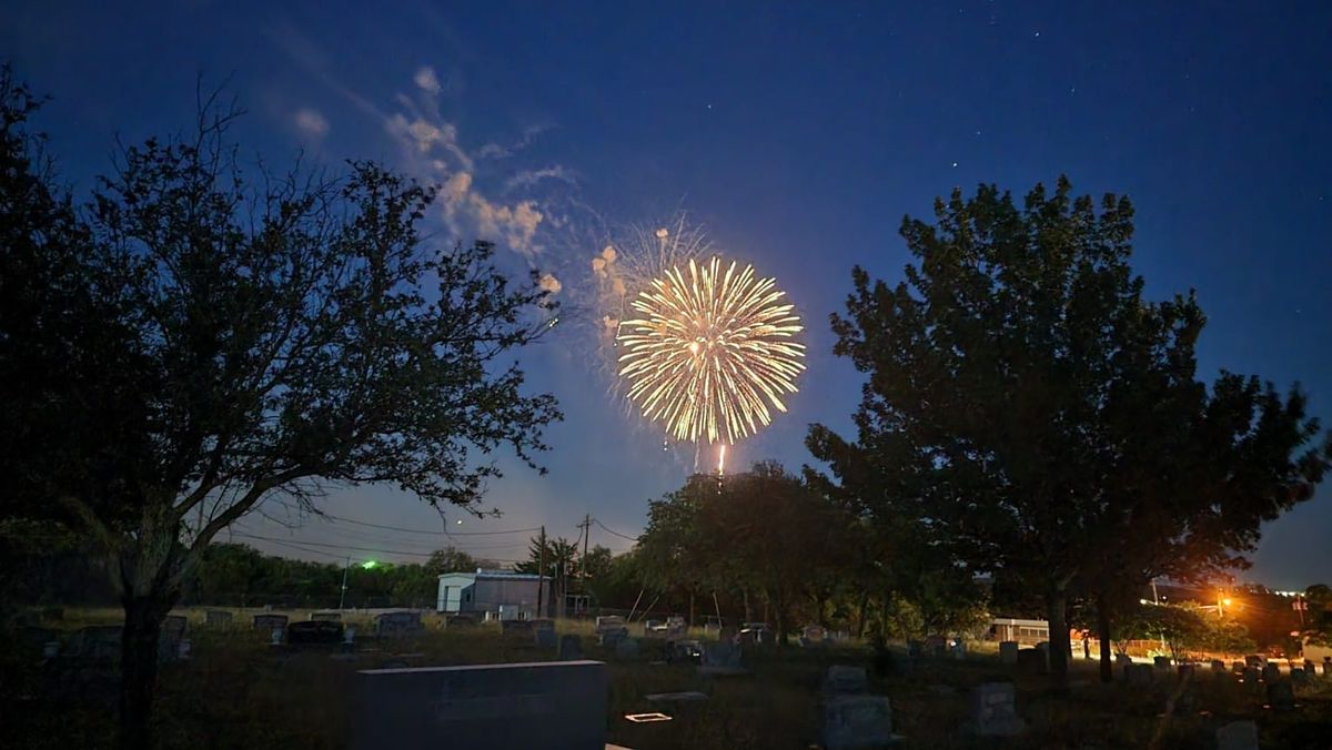 Fireworks lighting the night sky above trees and Oakwood cemetery.