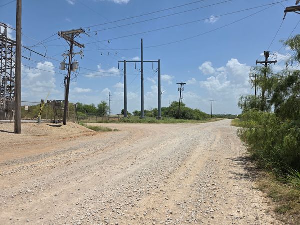 A fenced electrical substation and utility lines beside a rural Jack County gravel road under a blue sky.
