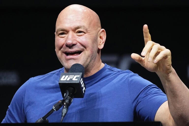 Dana White speaking into a UFC microphone with one finger raised during an event.
