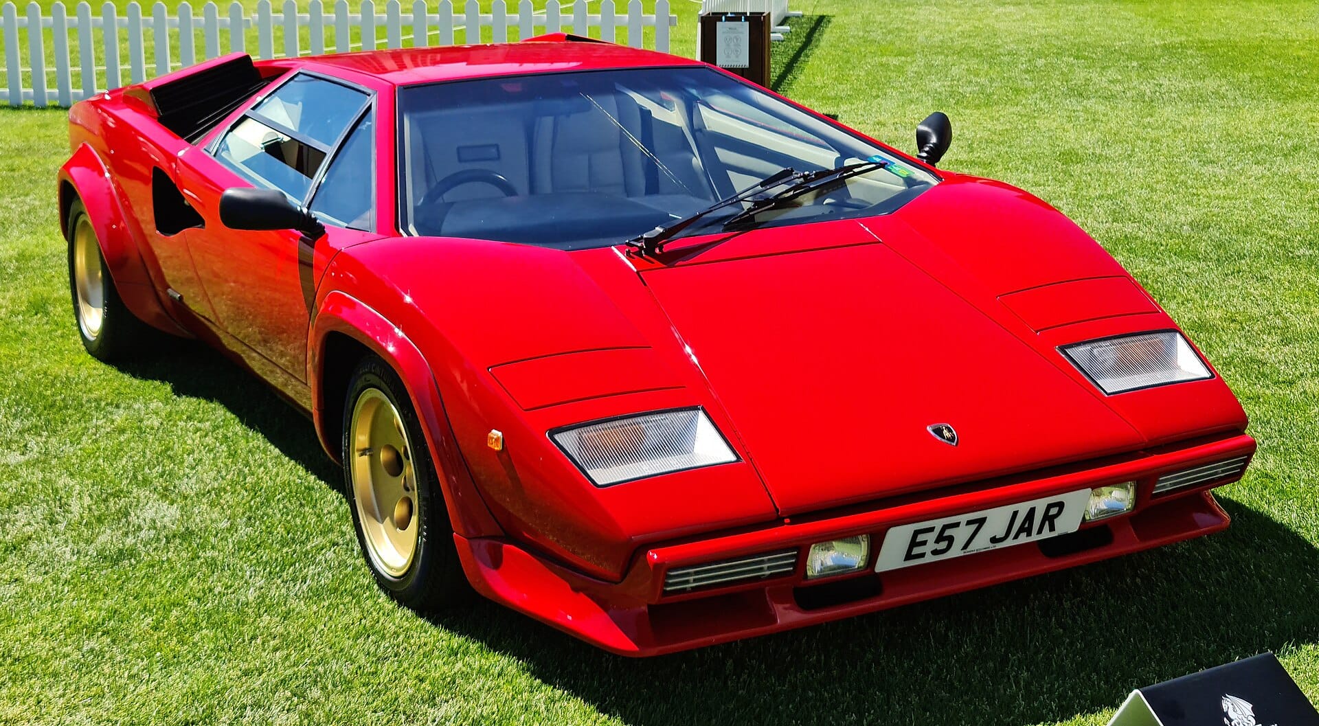 A bright red 1987 Lamborghini Countach 5000 QV with UK registration E57 JAR, owned by Harry Metcalfe, parked on a manicured lawn.