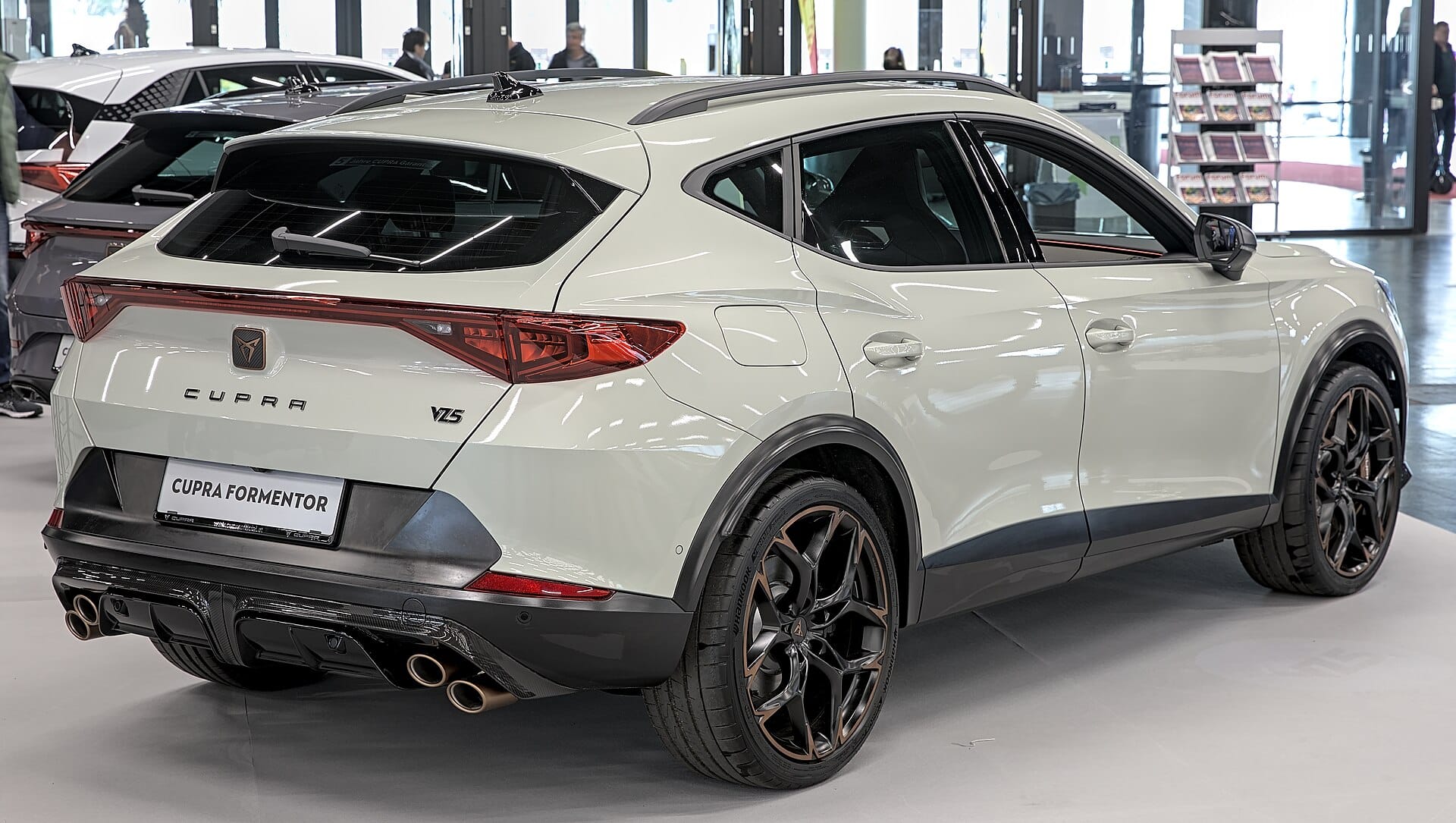 A rear three-quarter view of a white Cupra Formentor VZ5 displayed inside a showroom, showcasing its distinctive quad exhaust tips, copper-accented wheels, and rear badging.