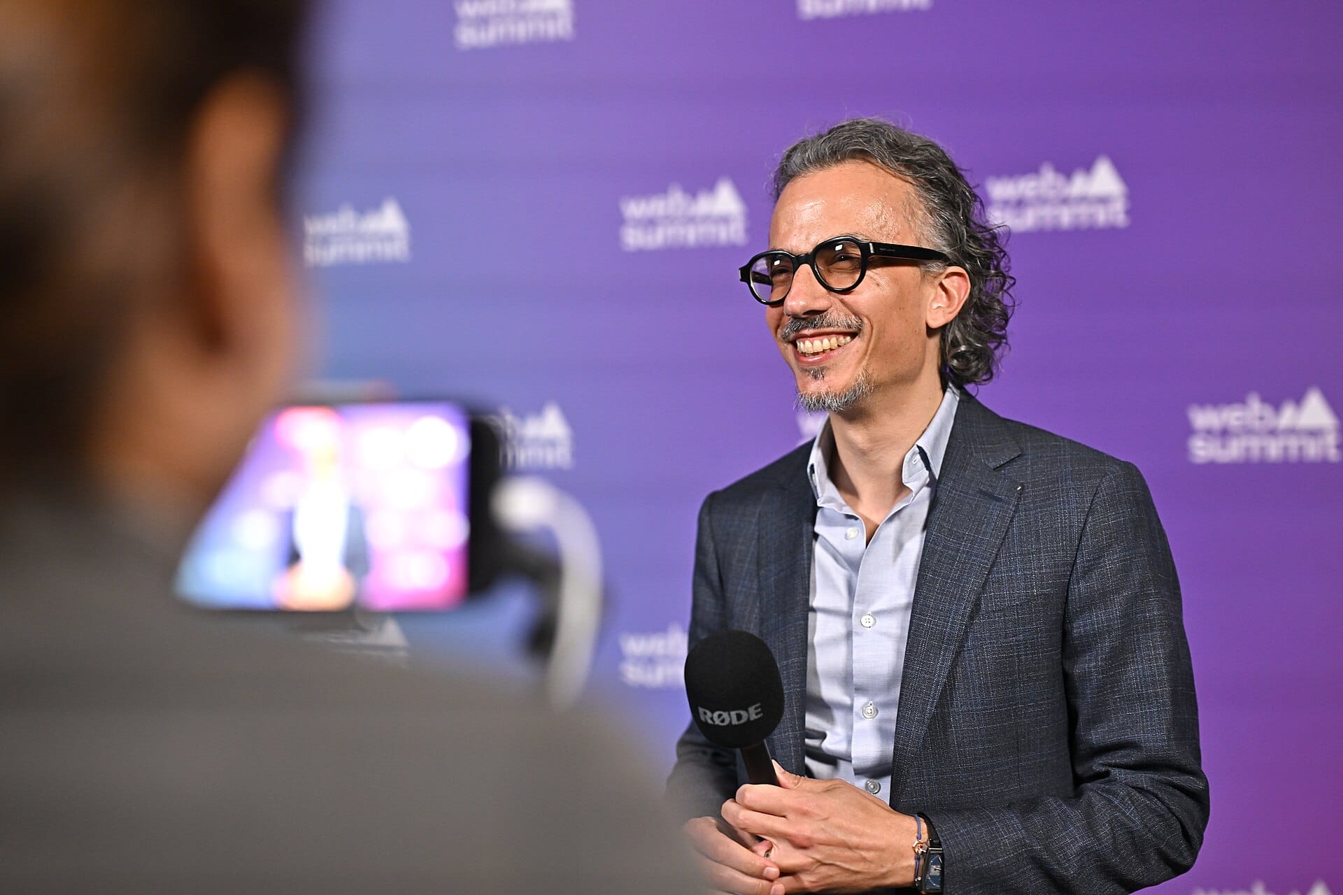 A medium shot of Laurent Mekies smiling while being interviewed in front of a Web Summit purple backdrop.