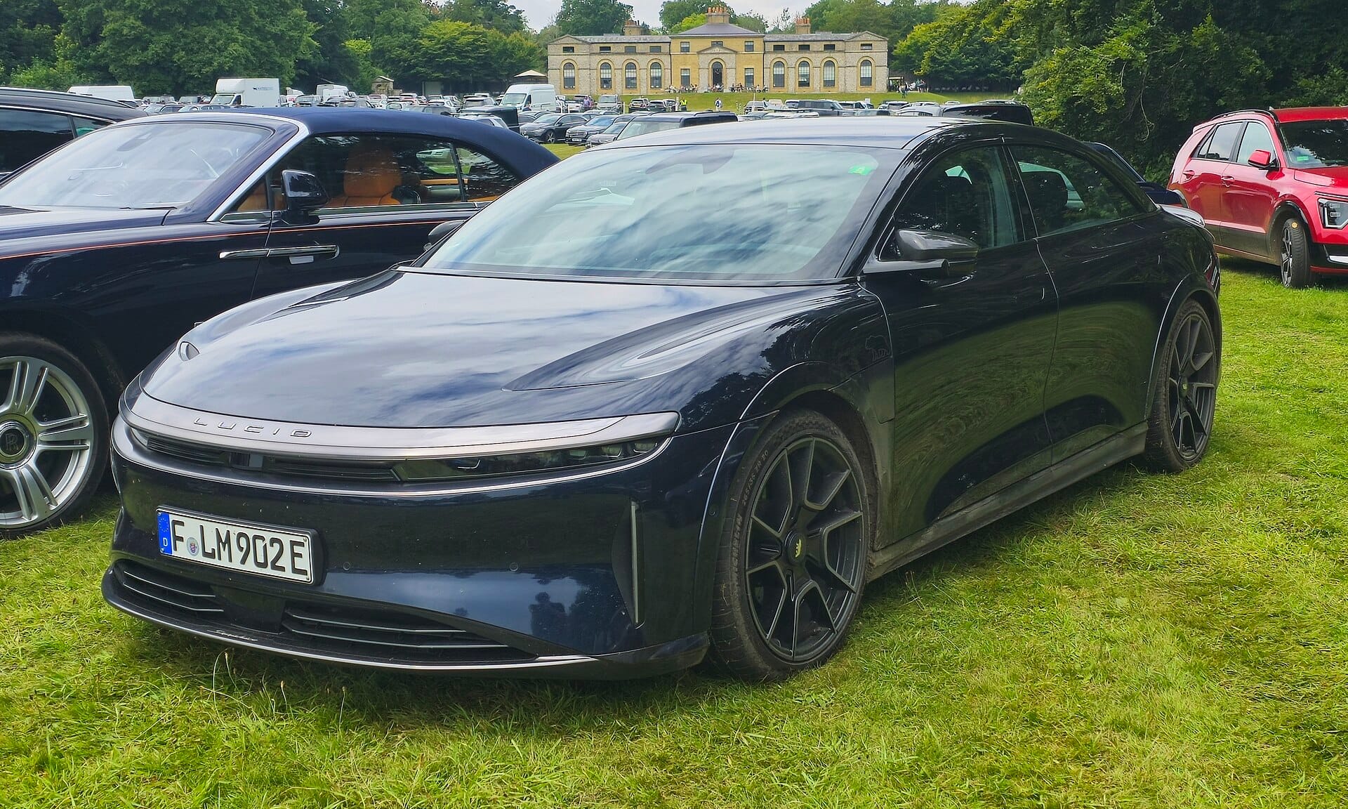 A dark blue Lucid Air Sapphire electric sports sedan parked on grass at an outdoor car event, shown from a front three-quarter perspective.