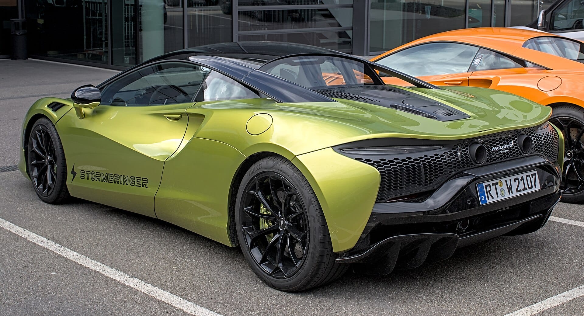A metallic green McLaren Artura sports car parked outdoors, shown from a rear three-quarter perspective.