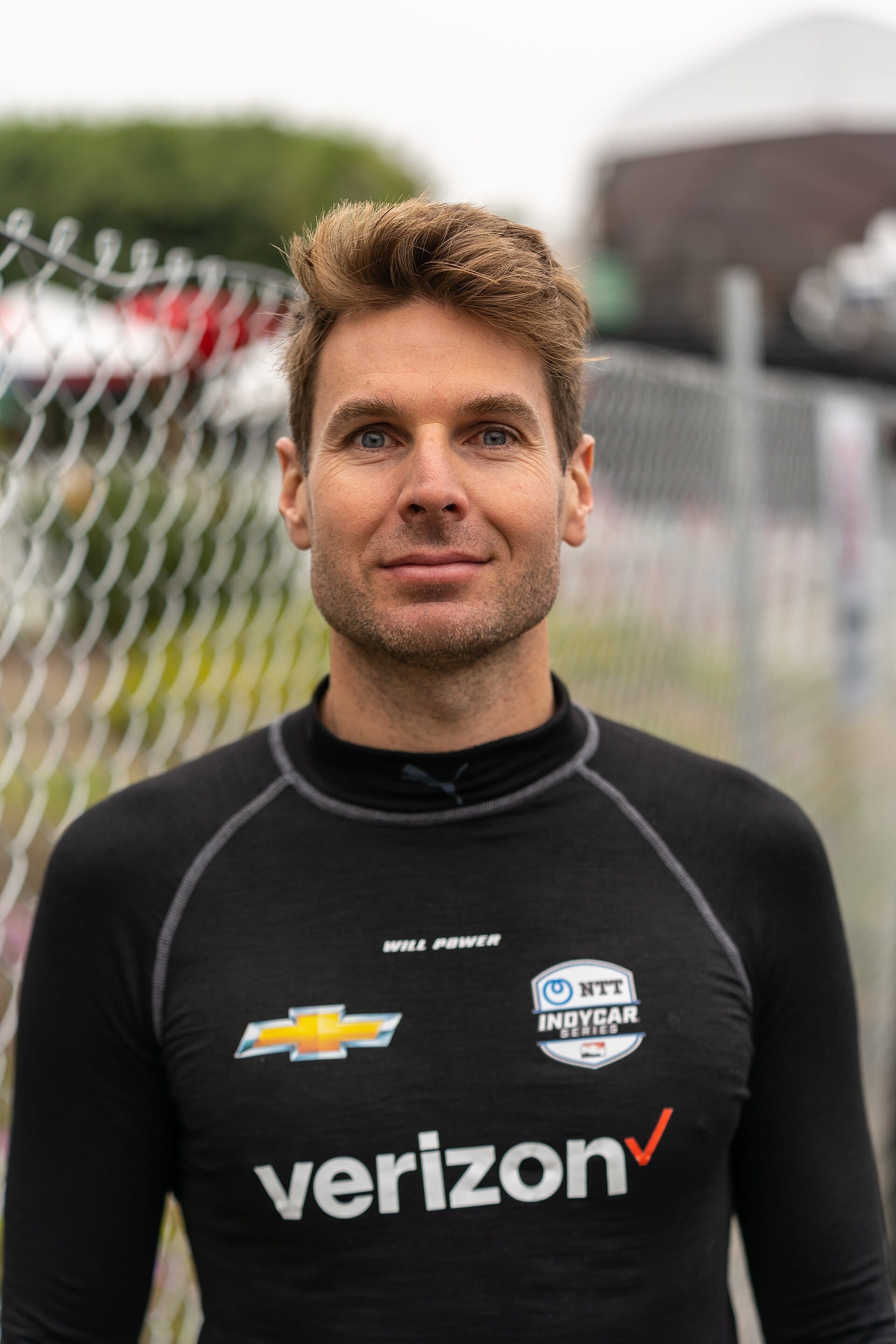 A close portrait of IndyCar driver Will Power wearing a black racing undershirt featuring the NTT IndyCar Series logo.