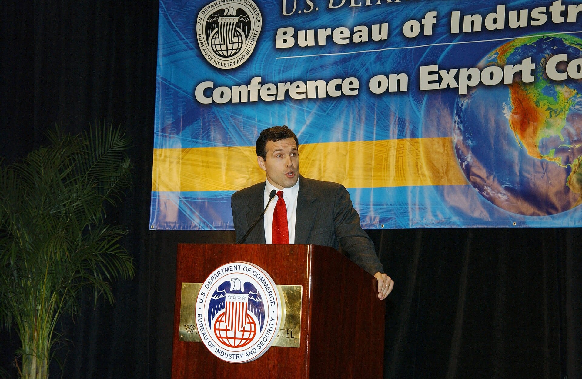 A speaker delivering a speech at a Bureau of Industry and Security conference behind a branded podium.
