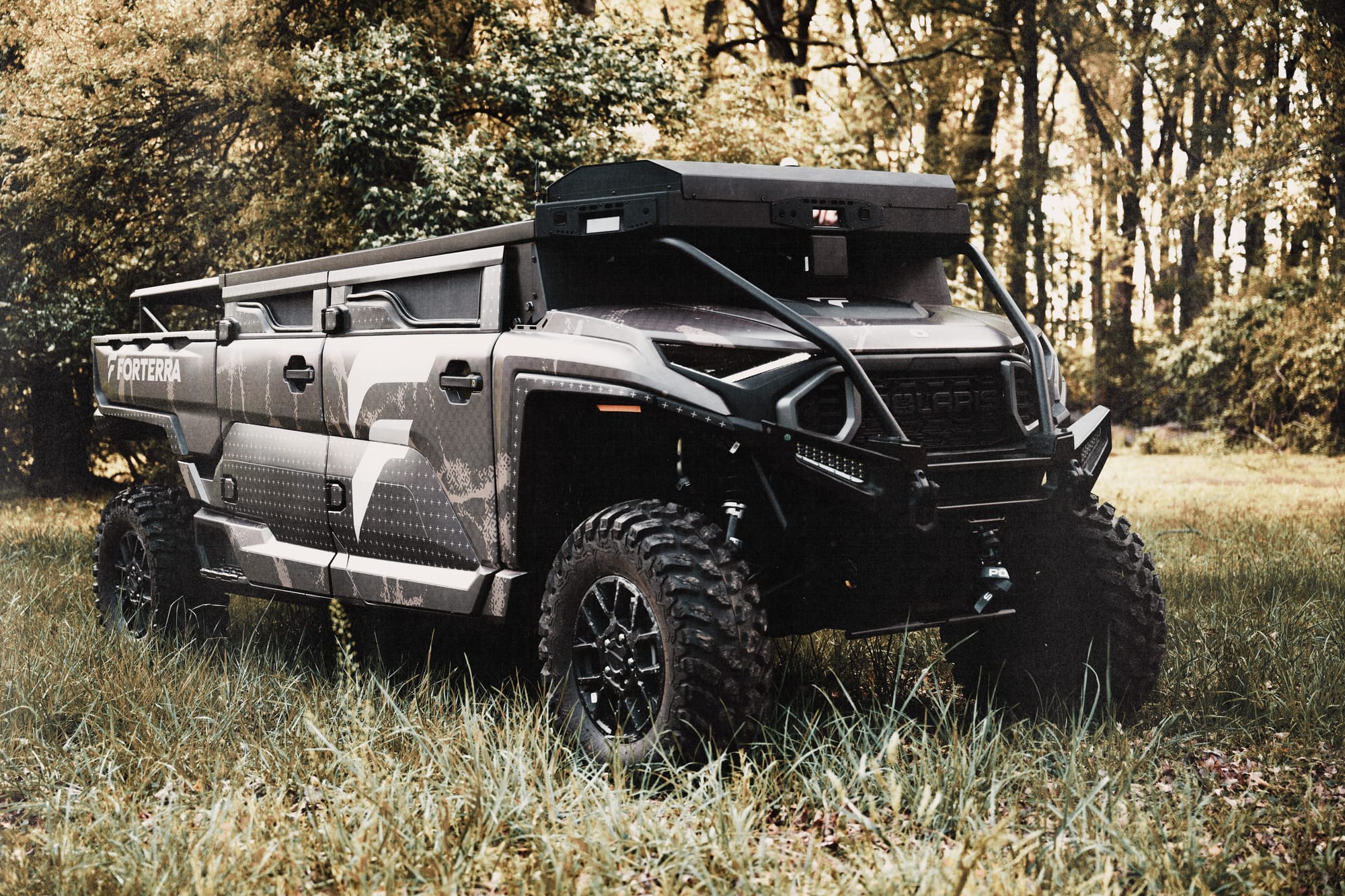 A rugged tactical off-road vehicle with Forterra branding parked in a grassy field near a forest.