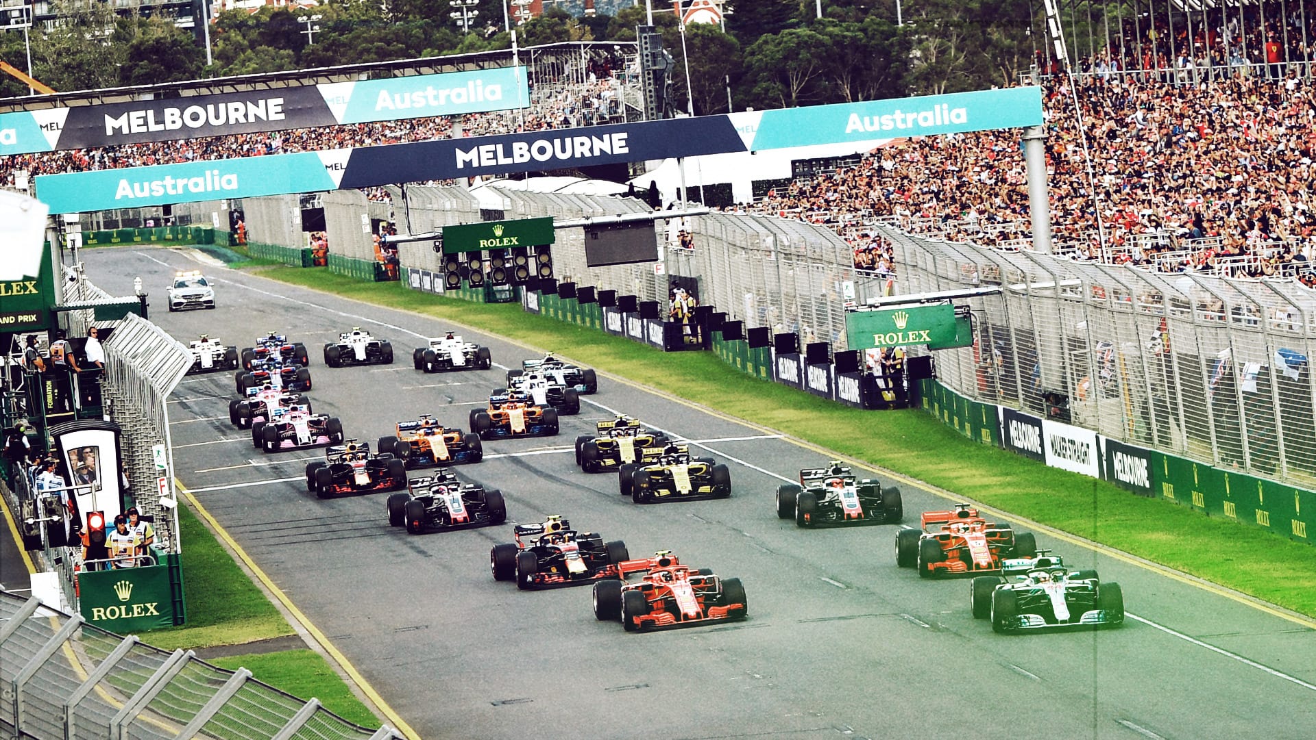 A high-angle shot showing Formula 1 race cars accelerating down the main straight grid under the Melbourne banner during the Australian Grand Prix.