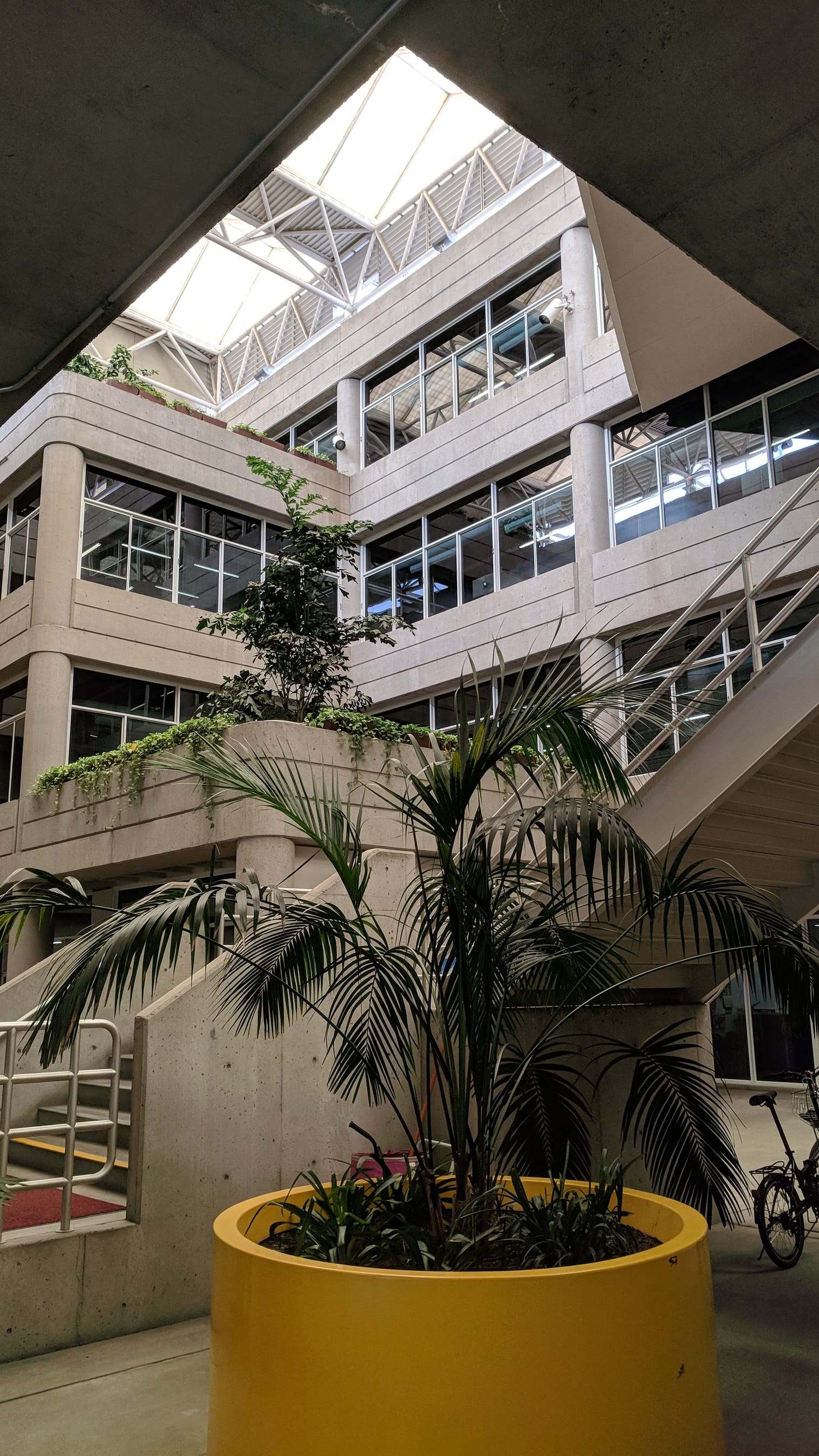 An interior view looking up at the multi-story atrium of the California Energy Commission building, featuring potted plants, concrete balconies, staircases, and a skylight.