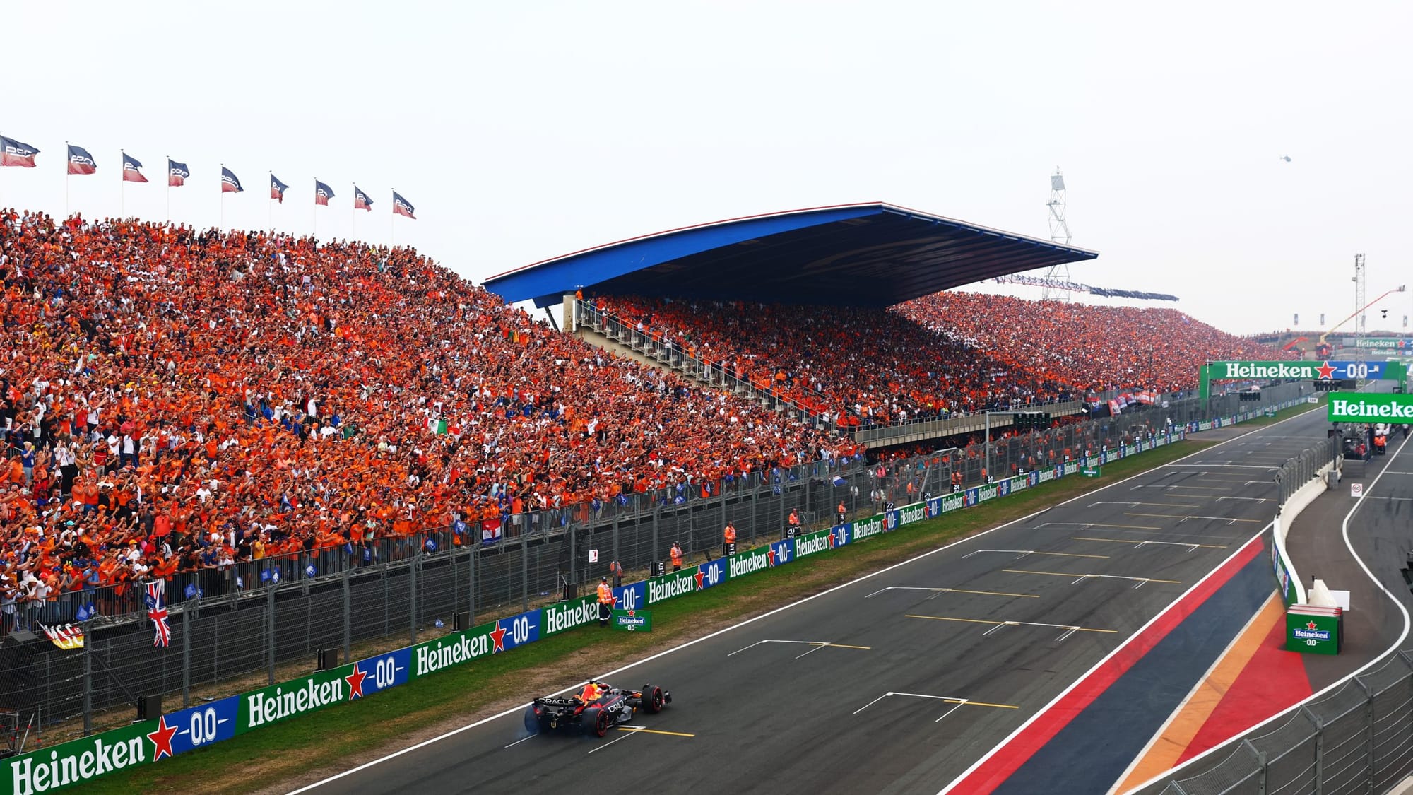 Wide shot of a Red Bull Formula 1 car driving along a racetrack in front of grandstands packed with orange-clad spectators.
