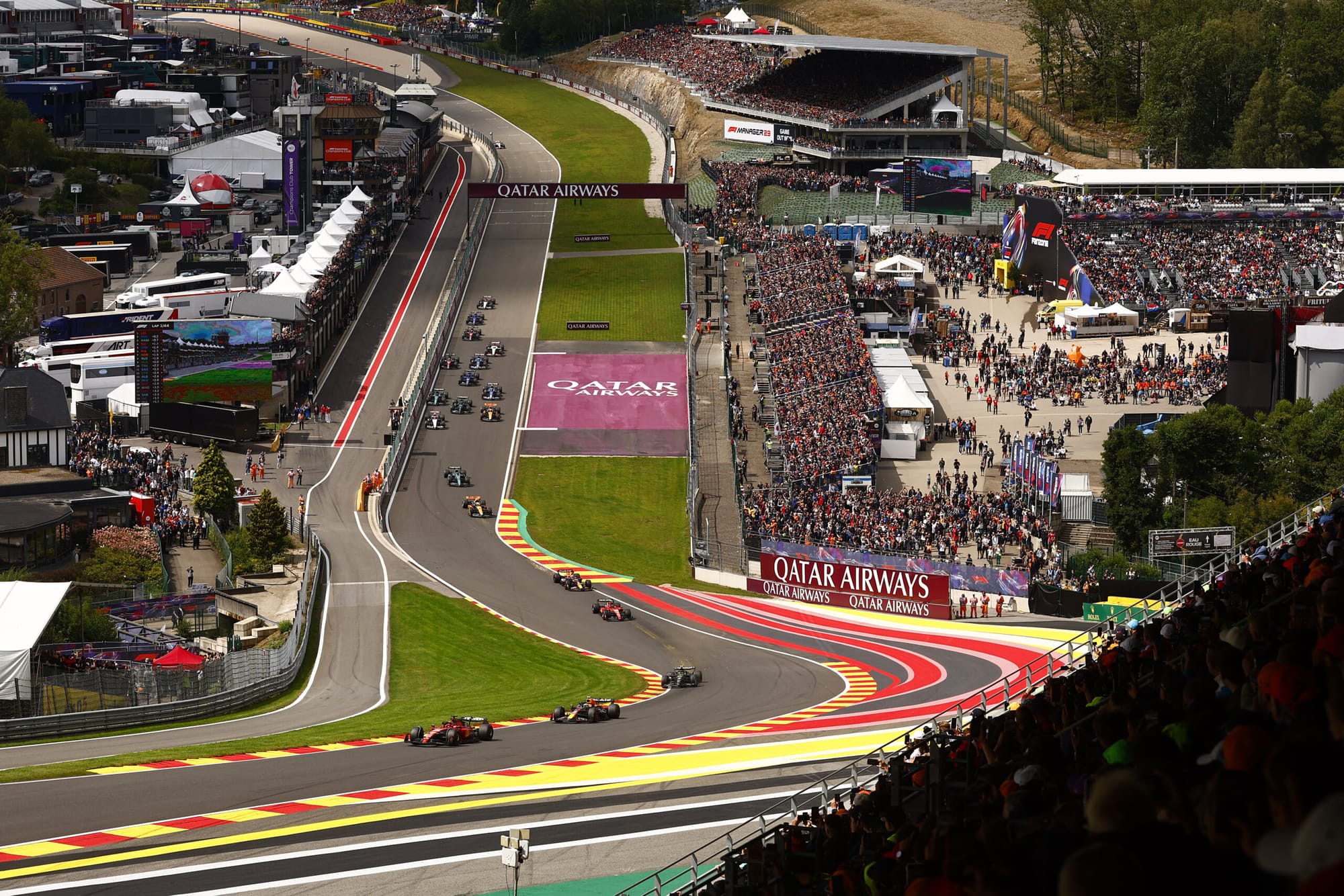 An elevated wide shot of Formula 1 cars navigating the Eau Rouge and Raidillon turns at the Circuit de Spa-Francorchamps.