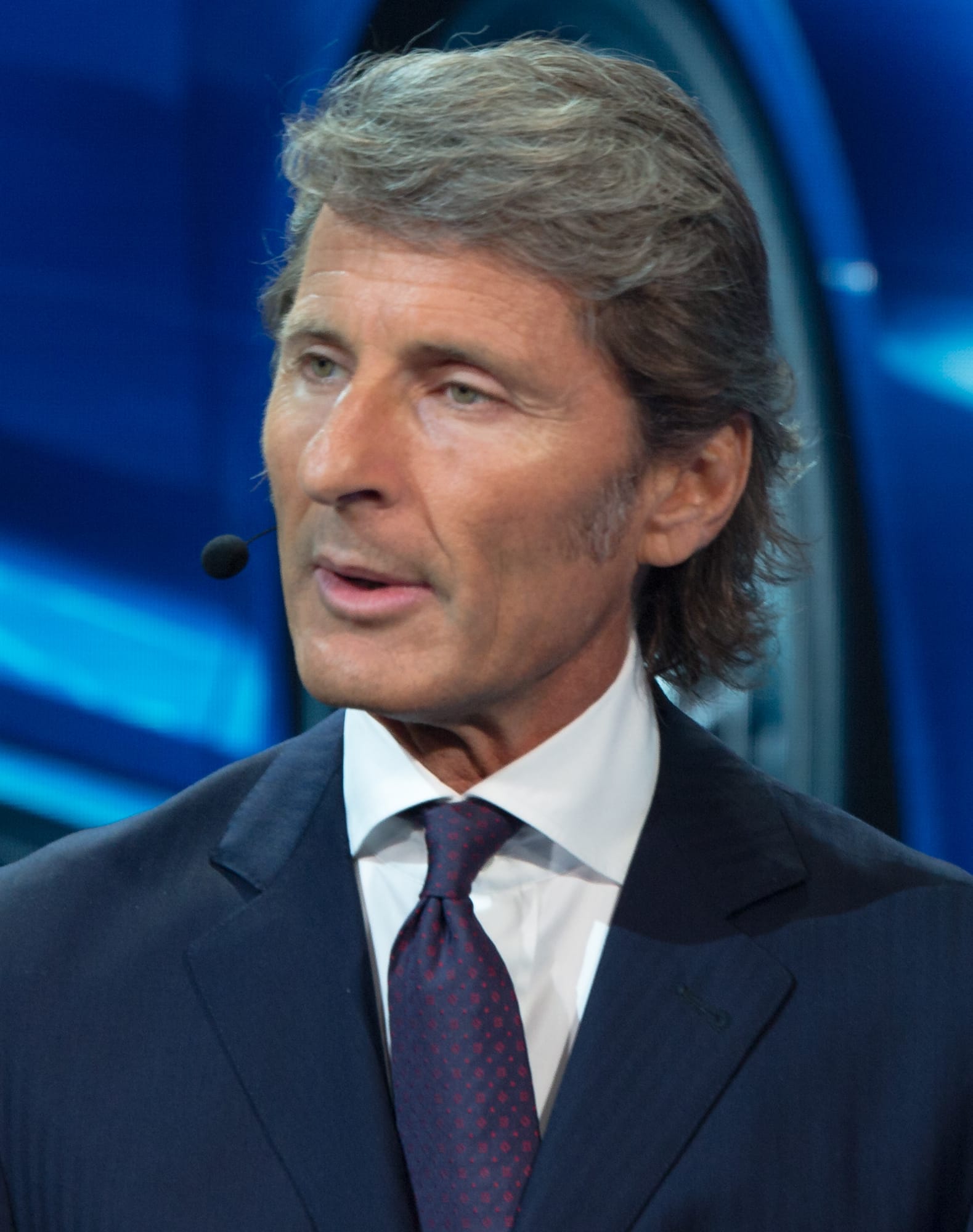 A close-up portrait of Stephan Winkelmann in a suit and tie with a headset microphone.