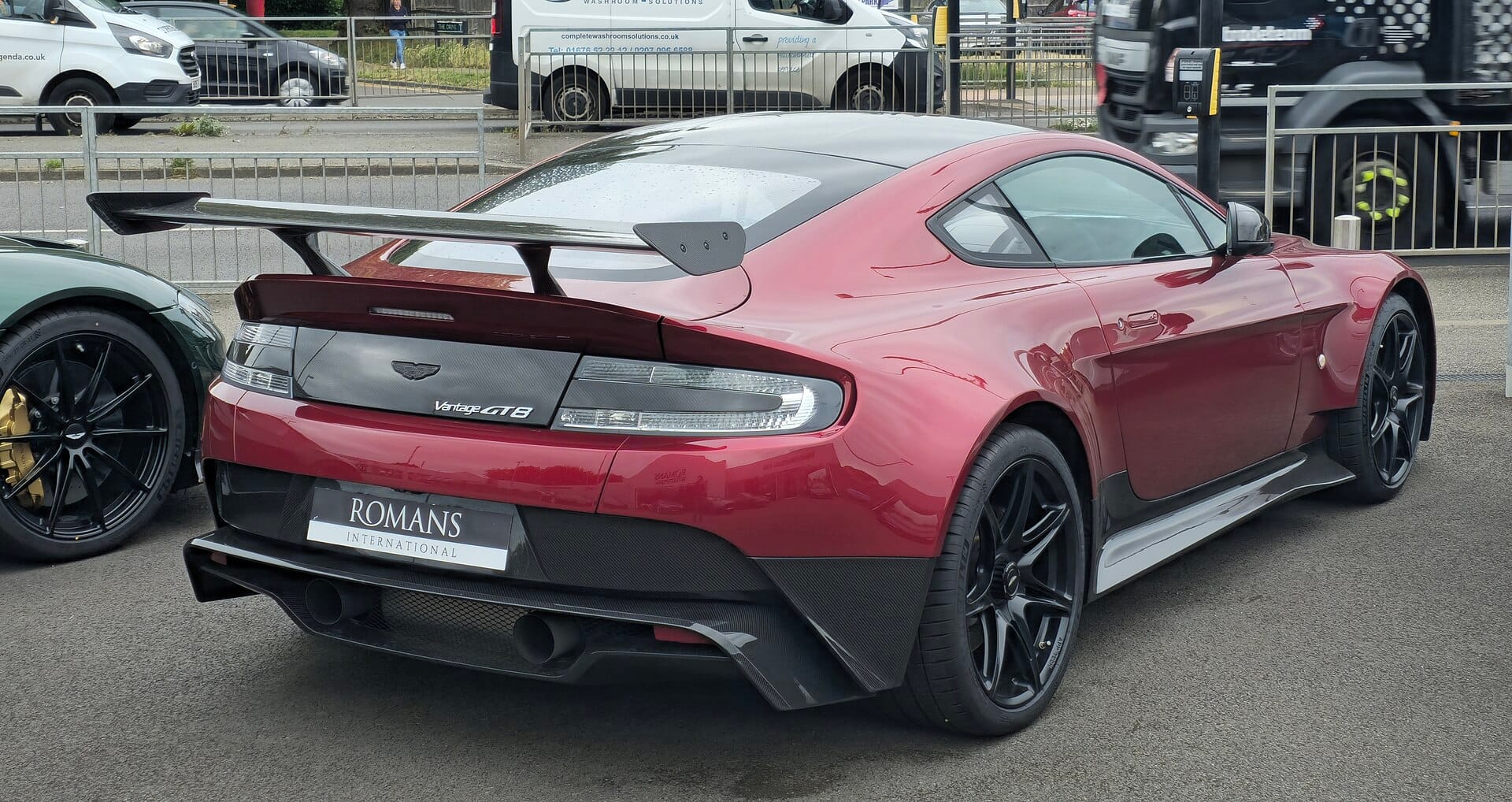 A rear three-quarter view of a red Aston Martin Vantage GT8 parked outdoors, featuring carbon fiber aerodynamic elements and a large rear wing.
