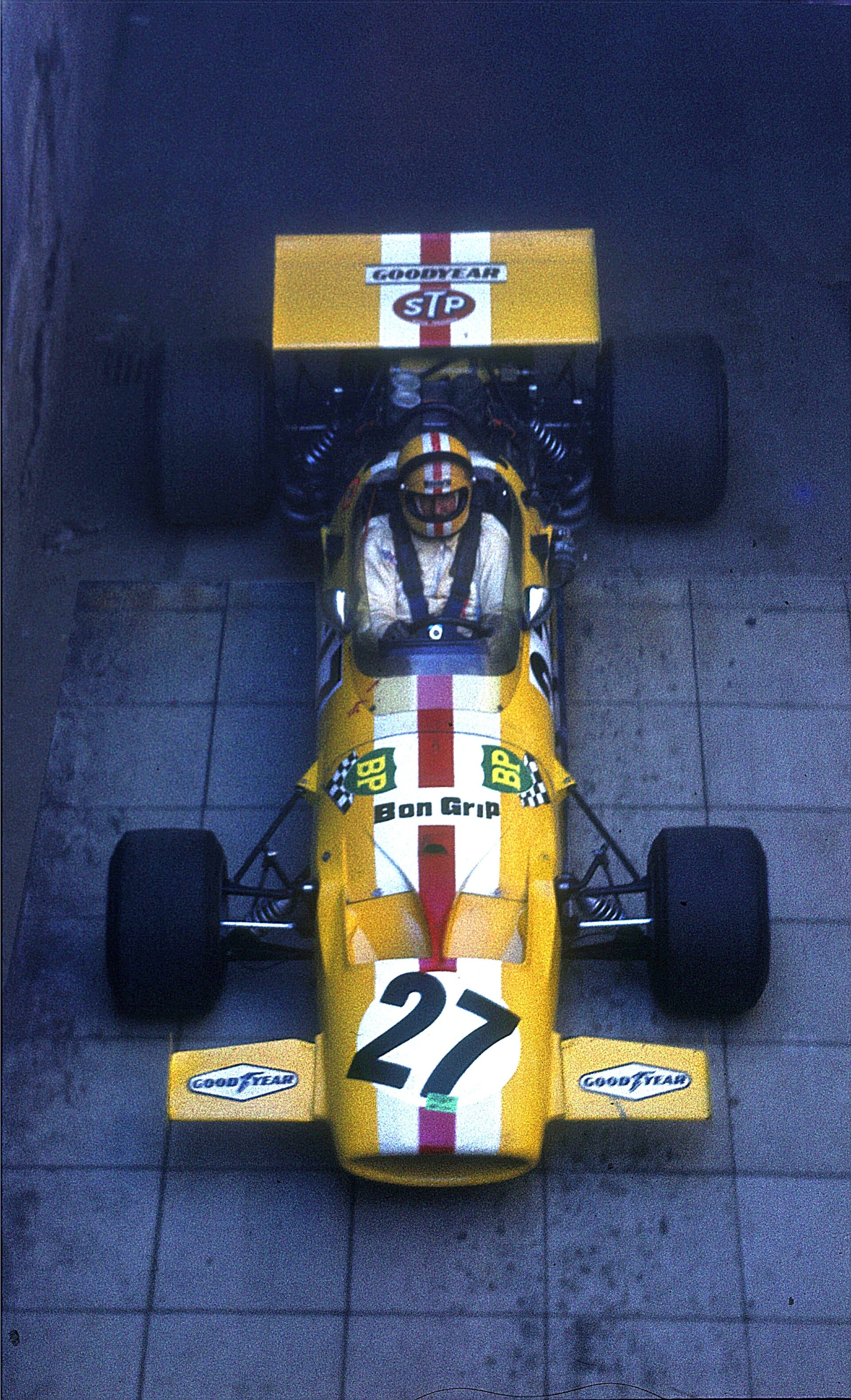 An overhead shot of a classic yellow and white McLaren Formula 1 race car, numbered 27, with a driver seated inside.