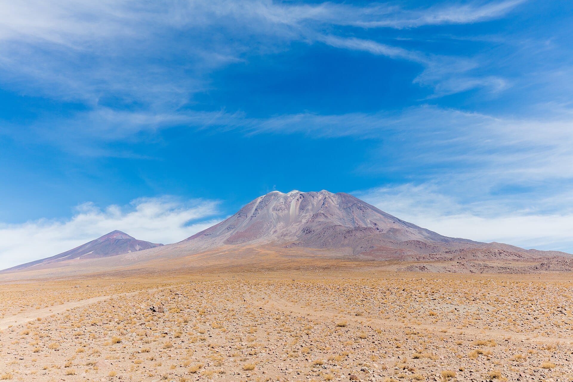 A wide shot of a desert landscape in Chile featuring a massive volcano under a blue sky with wispy clouds.