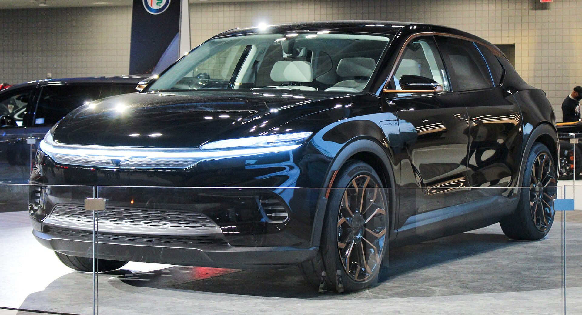 A front three-quarters shot of a black Chrysler Airflow concept vehicle displayed indoors at an auto show.