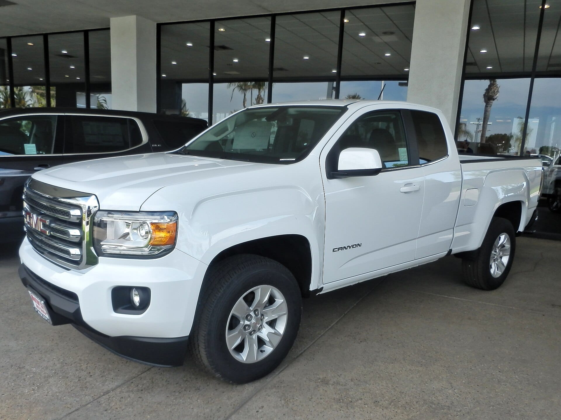 A white GMC Canyon pickup truck parked outside a building with large windows.