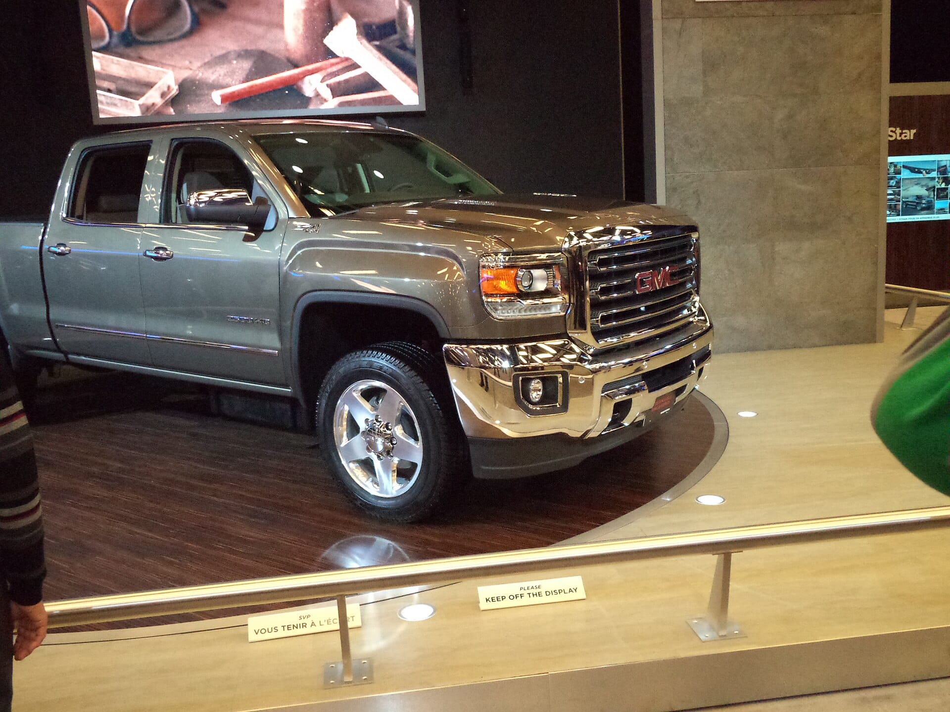 A bronze GMC Sierra HD pickup truck on display at an auto show or showroom, viewed from a front three-quarter angle.