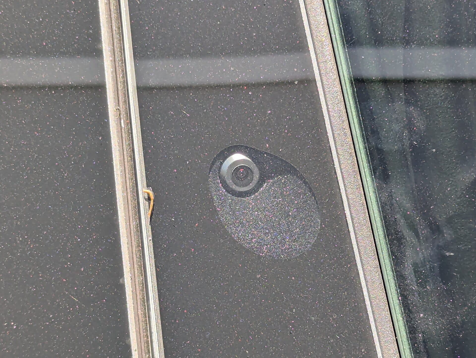 A close-up view of an exterior autopilot camera mounted on the B-pillar of a vehicle, typical of a Tesla Autopilot/FSD sensor.