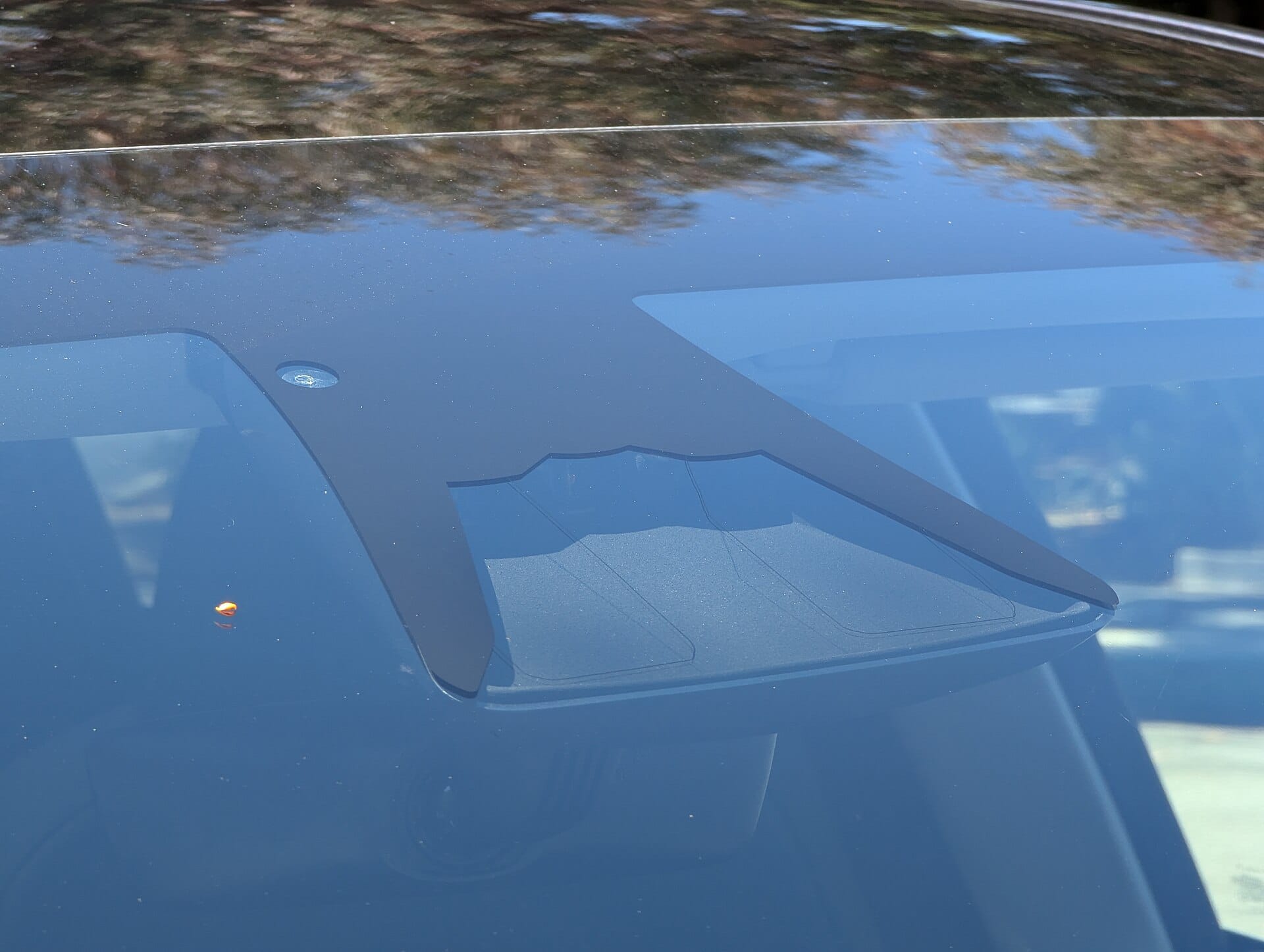 A close-up view of the windshield camera housing used for Tesla Autopilot and FSD systems, mounted near the rearview mirror.